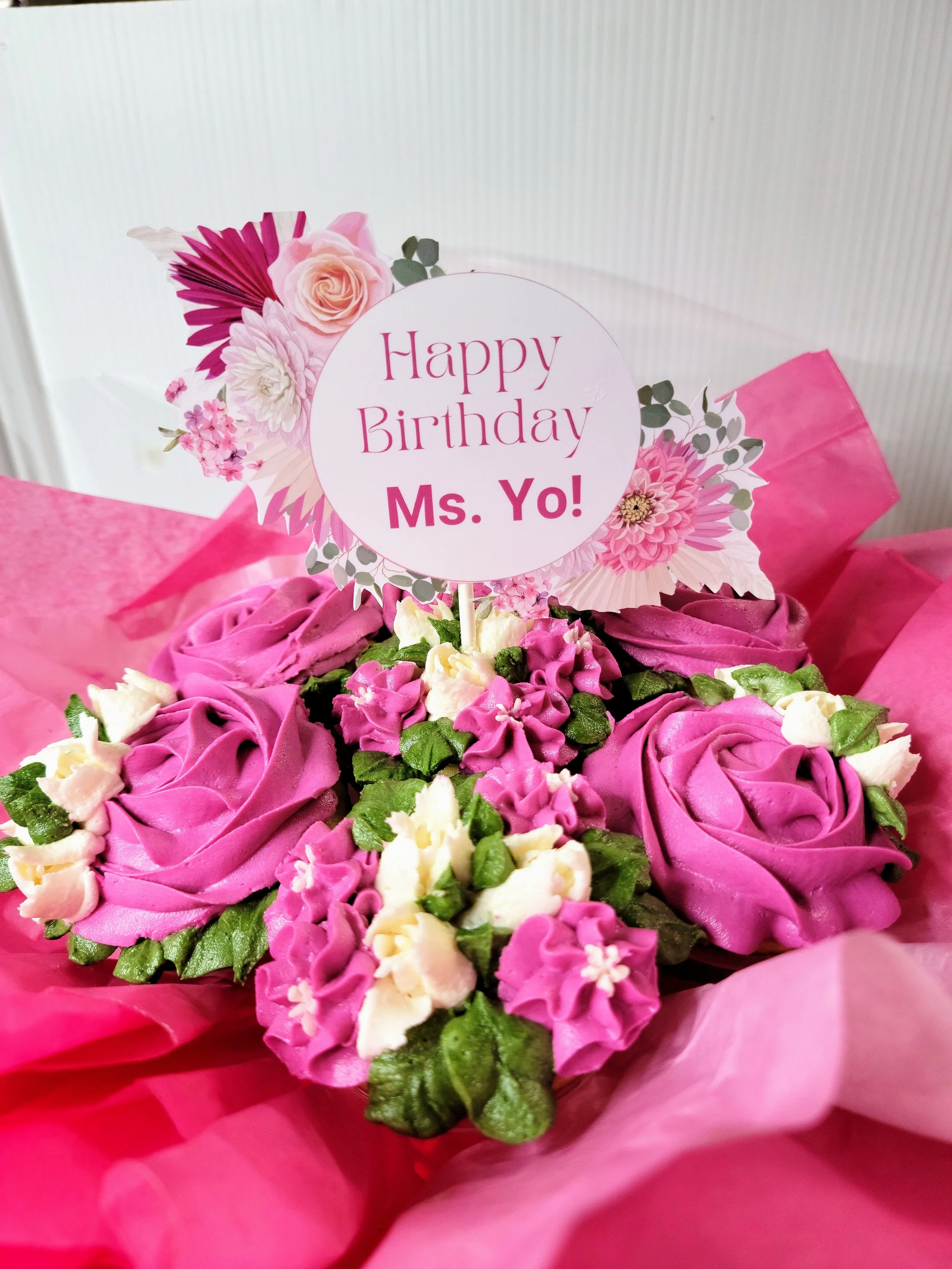 Pink and purple flower arrangement with a 'Happy Birthday Ms. Yo!' sign on top.