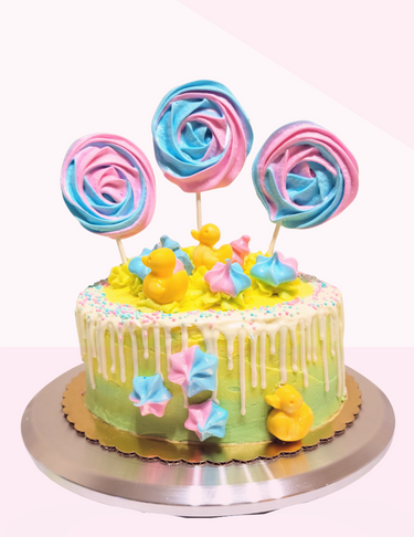 Colorful cake decorated with pastel-colored meringue lollipops, rubber duckies, and pastel frosting flowers.