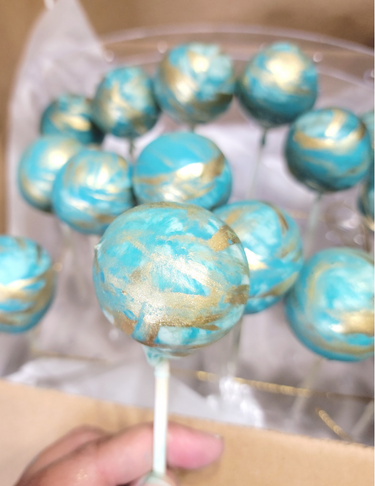 Multiple blue and gold marbled cake pops on a display stand.