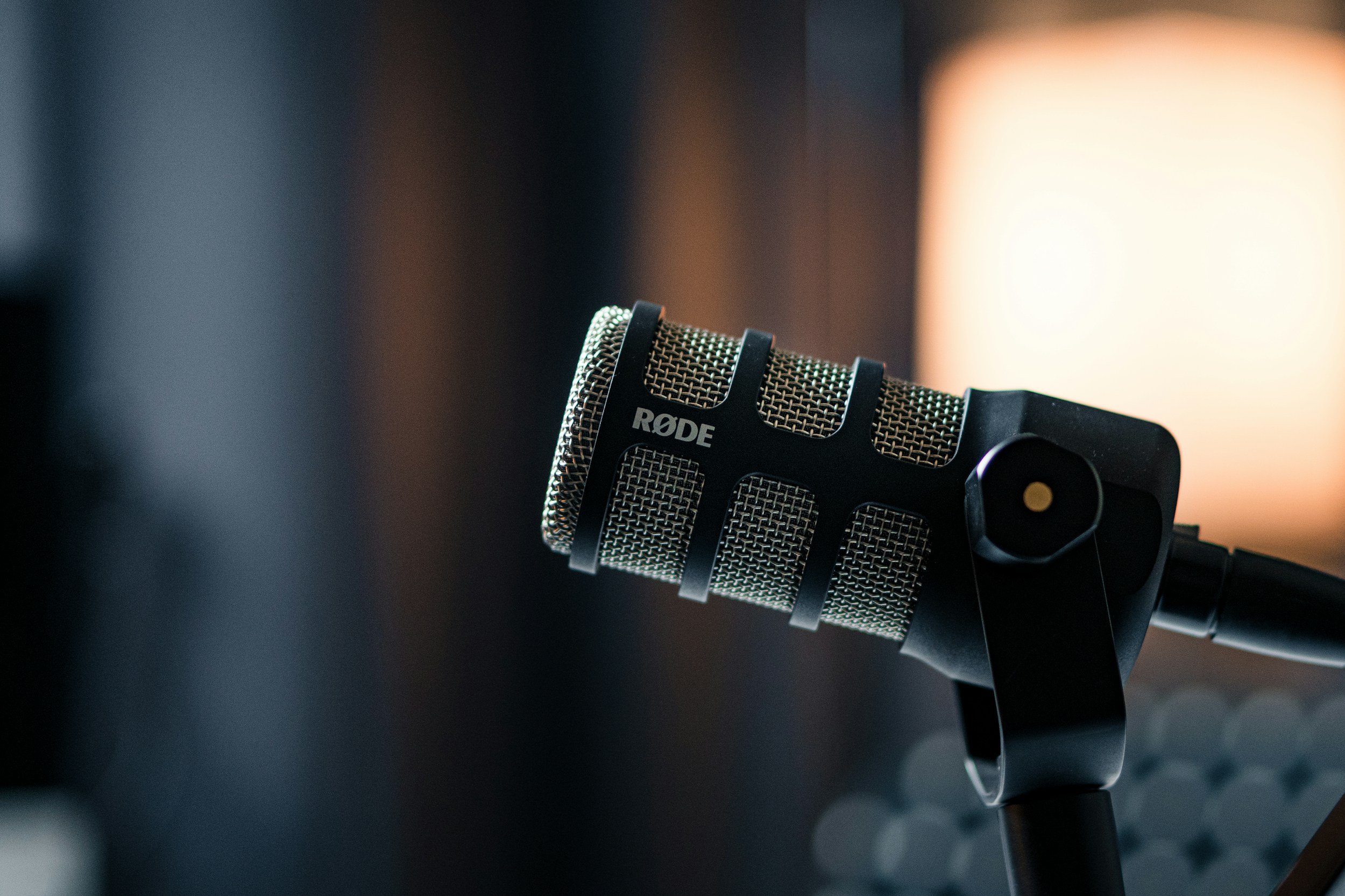 Close-up of a Rode microphone mounted on a stand, against a blurred background with warm lighting.