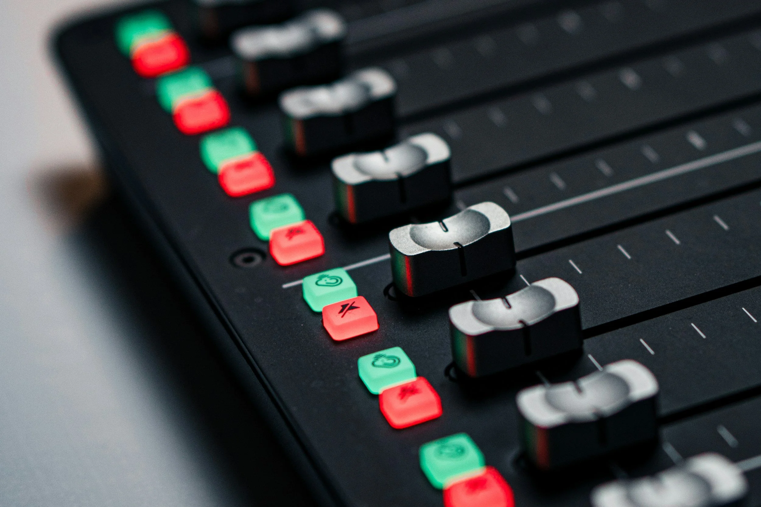 Close-up of a professional audio mixing console with faders, knobs, and illuminated buttons.