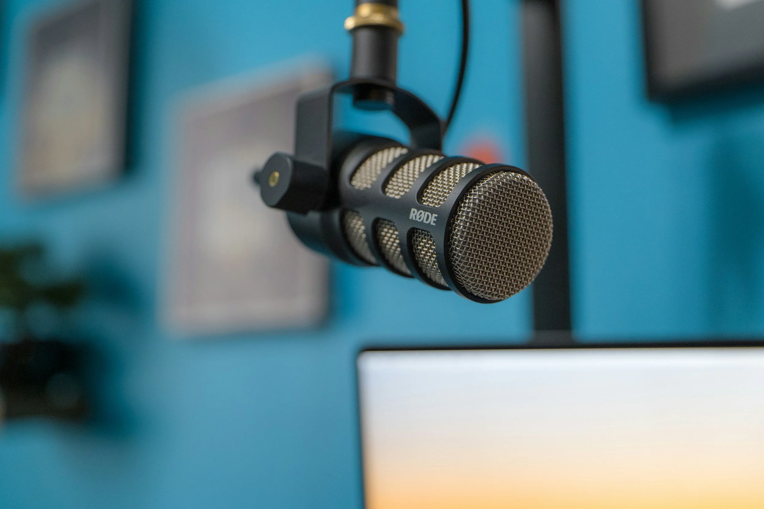 Close-up of a Rode microphone mounted on a stand, with a blurred background of blue and yellow hues.