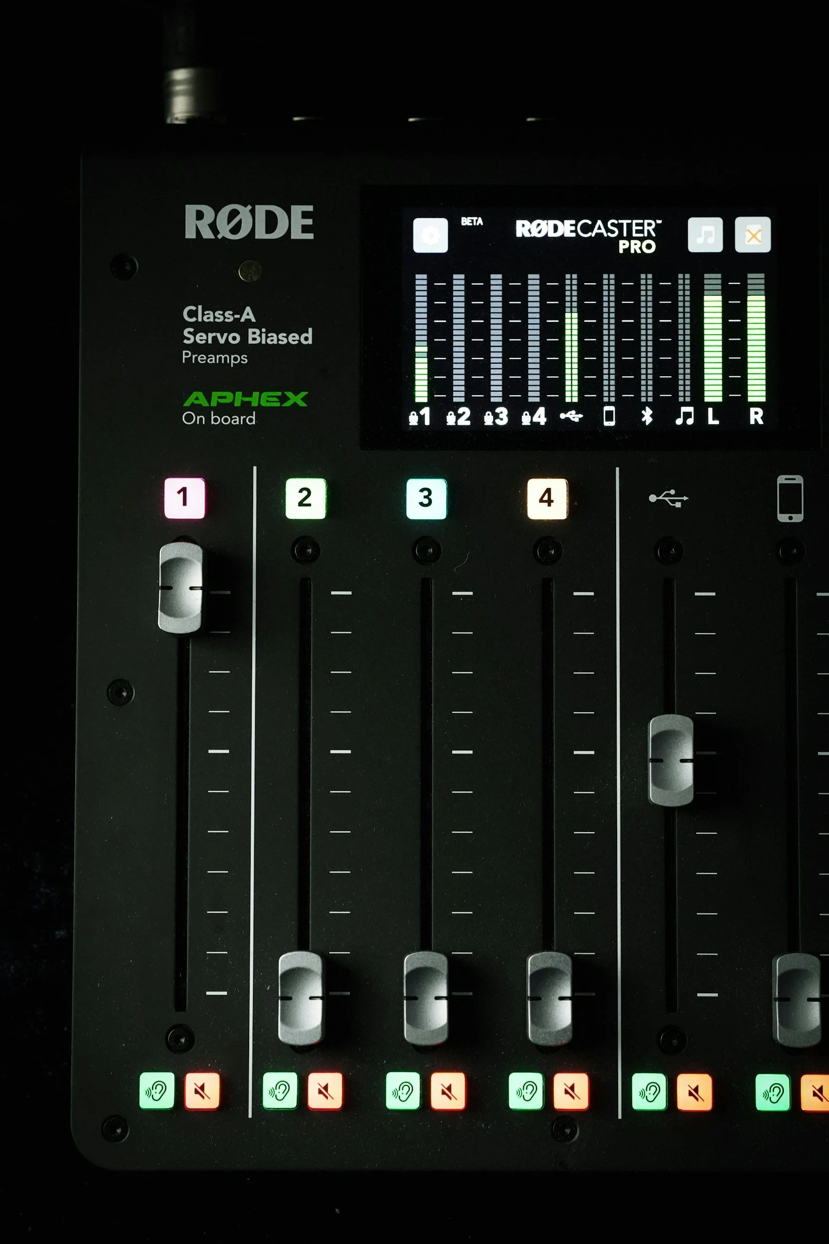 Close-up of a RODECaster Pro audio mixing console with volume faders, mute buttons, and a display screen showing audio levels and controls.