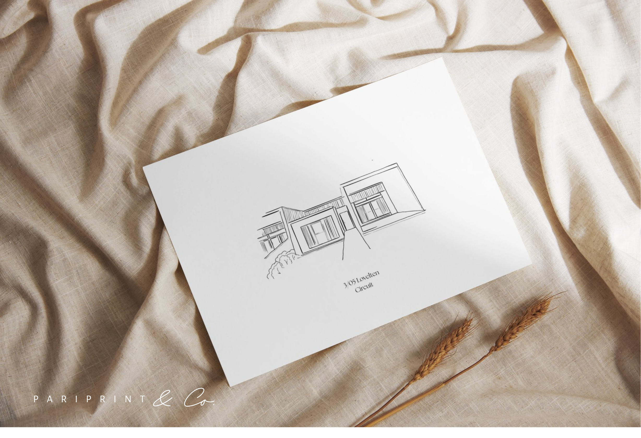 A white card with a line drawing of a modern house labeled '3/05 Lovetern Circuit' on a beige fabric background with two wheat stalks nearby.