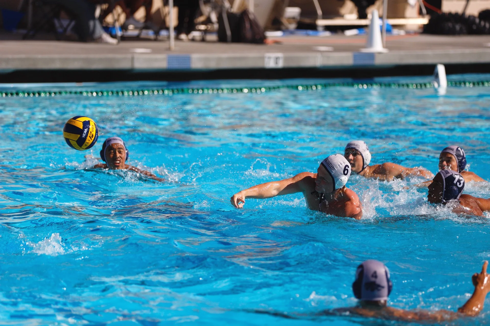 Water polo players competing in a pool, wearing caps and displaying intense effort during the game.