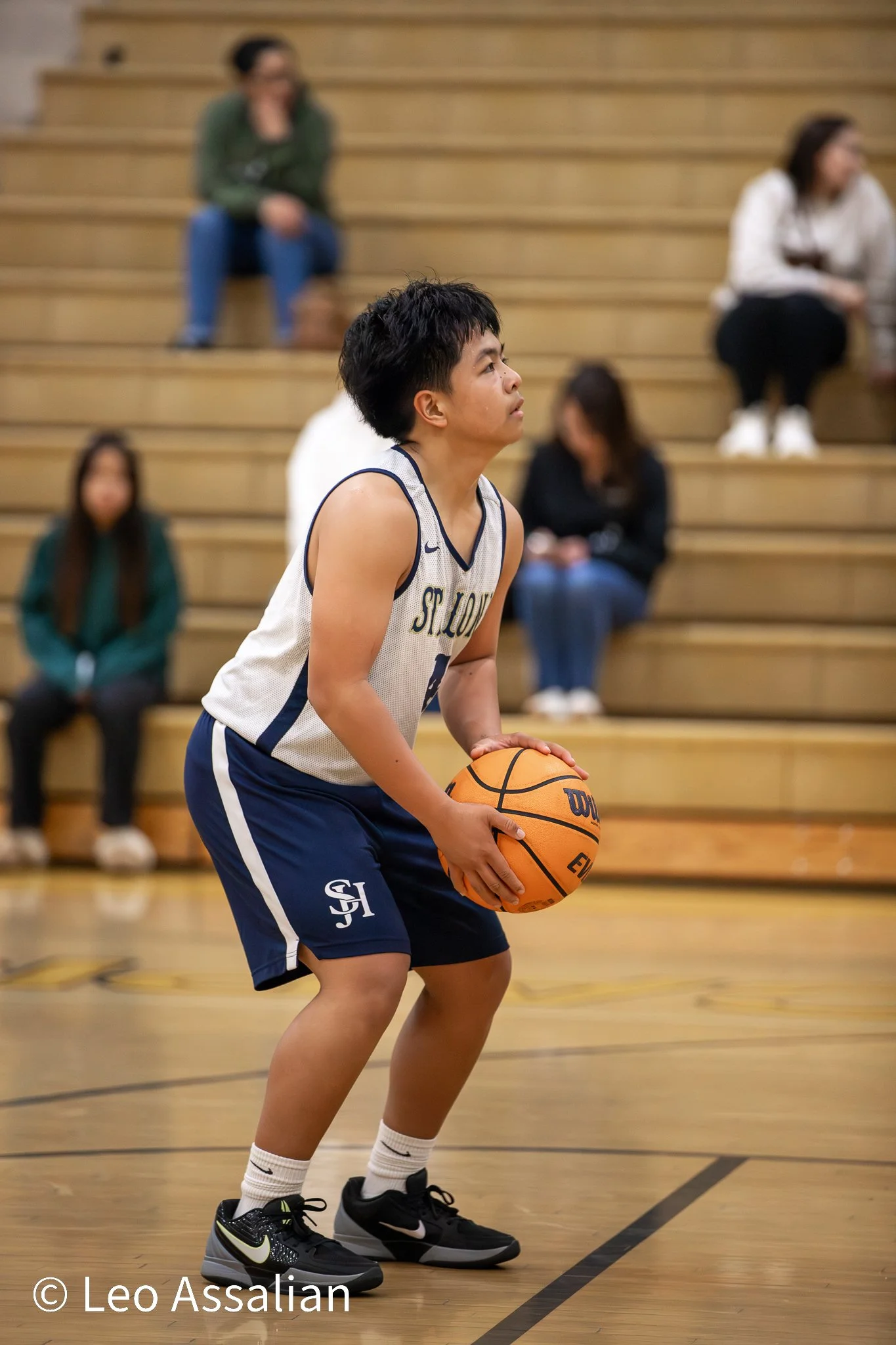 A young male basketball player in uniform holding a basketball on the court during a game or practice.