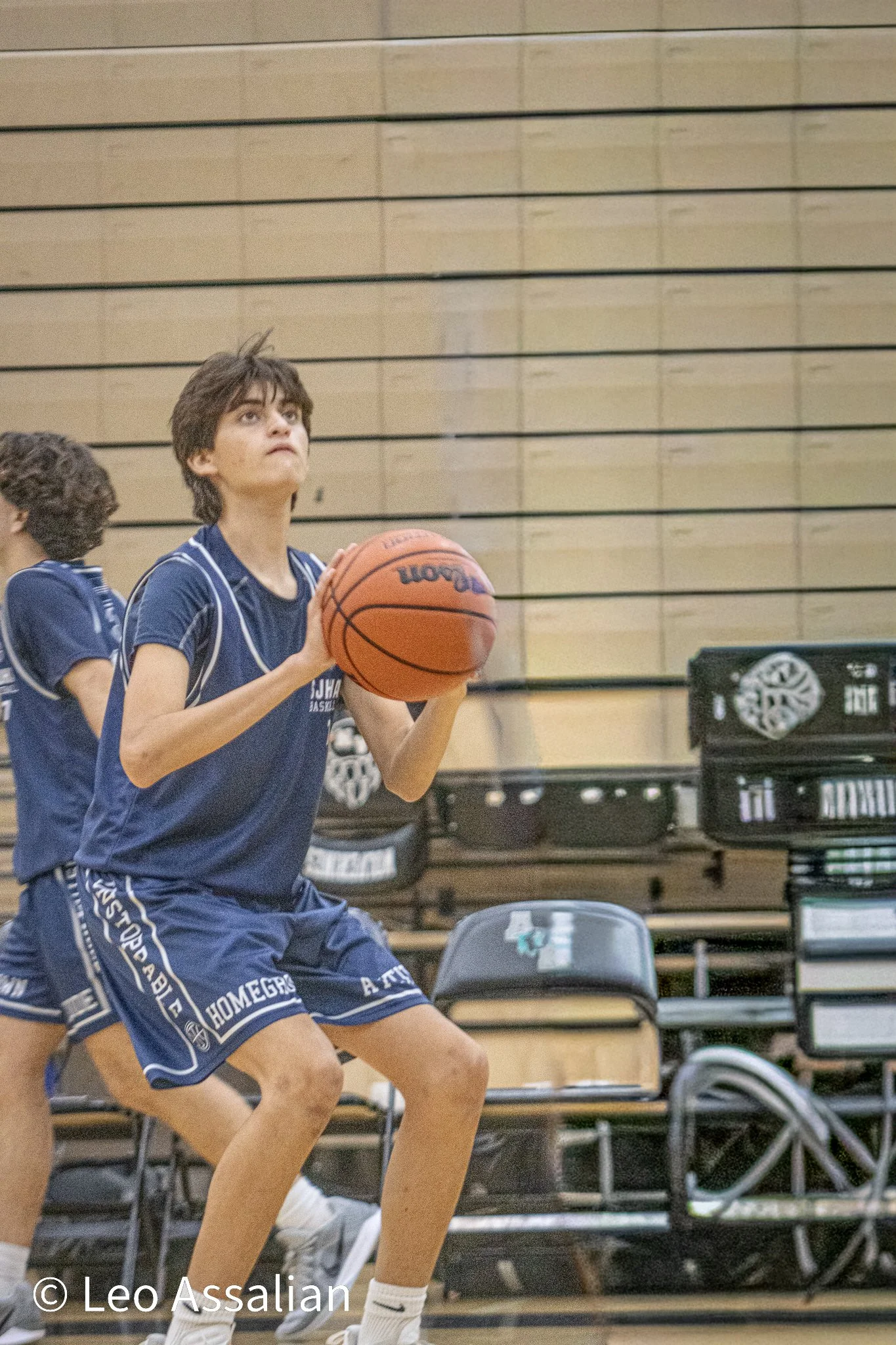 Young boys playing basketball in a gymnasium, with one boy preparing to shoot the ball. They are wearing blue team uniforms and sneakers.