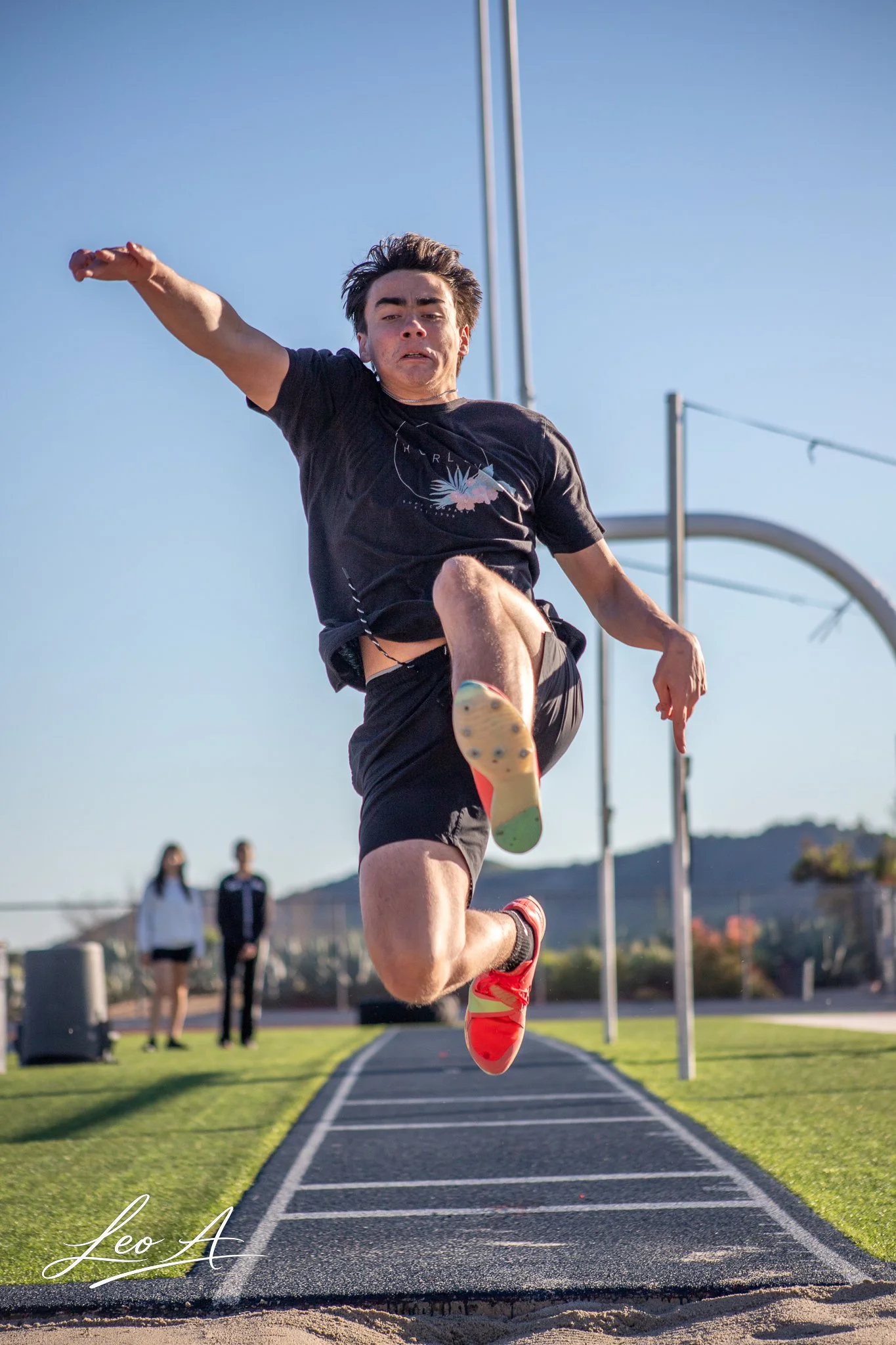 Sports portrait of young athlete in mid-air during long jump event at outdoor track and field stadium by photographer Leo Assalian.