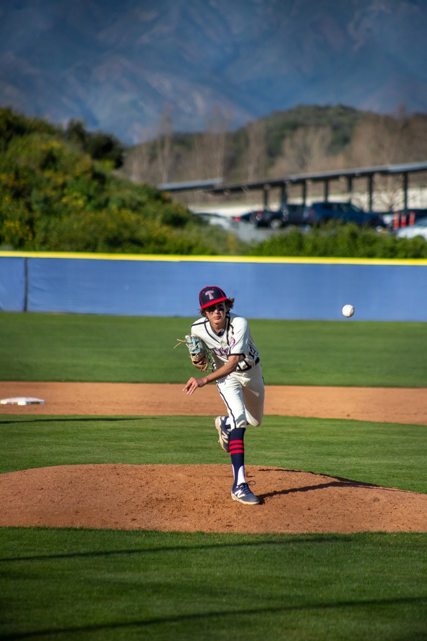 Sports portrait of a young baseball player in a white uniform pitches a ball on a baseball field by Leo Assalian.