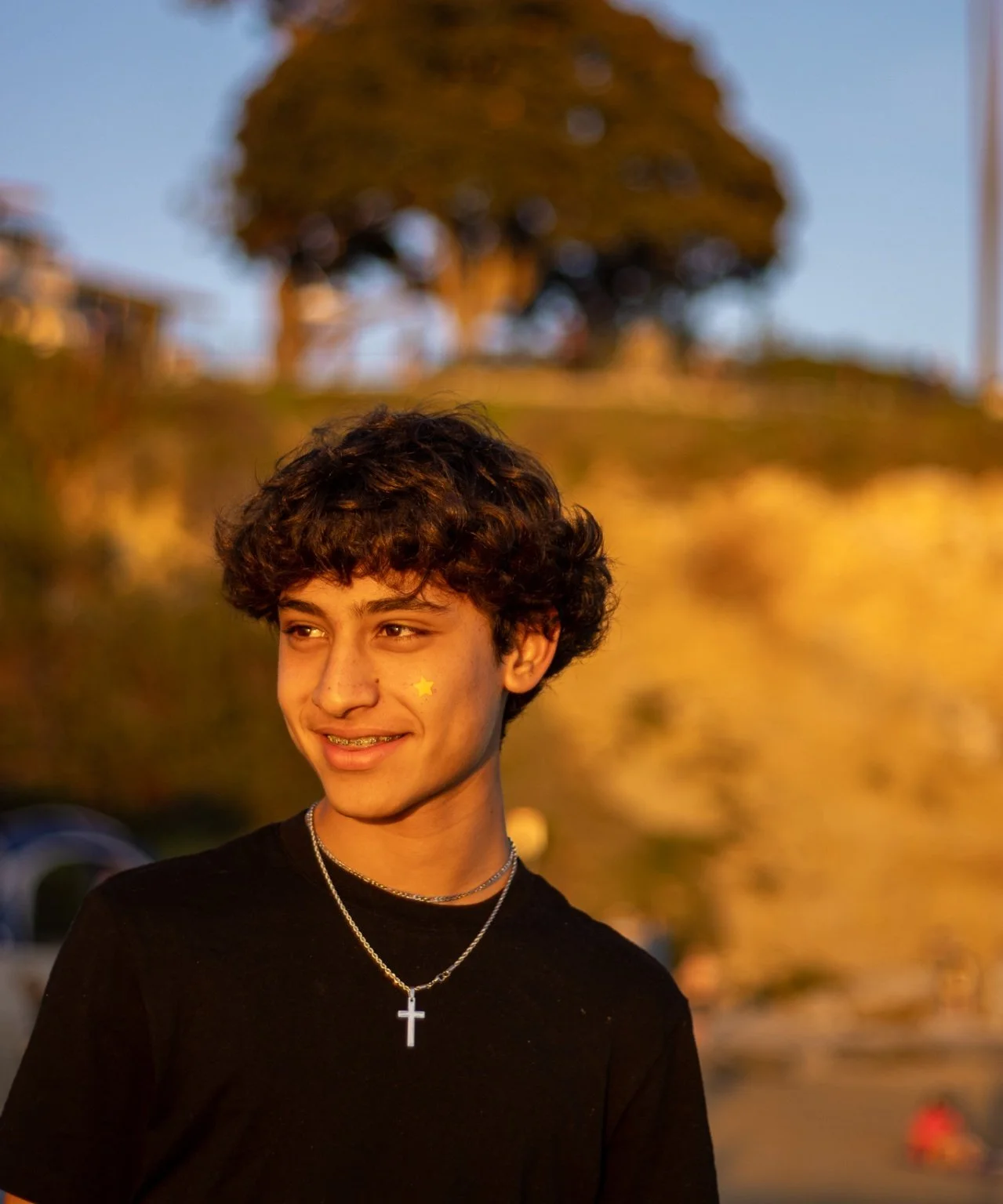 Portrait of a young man with curly hair, wearing a black tee, smiling during golden hour, by photographer Leo Assalian.
