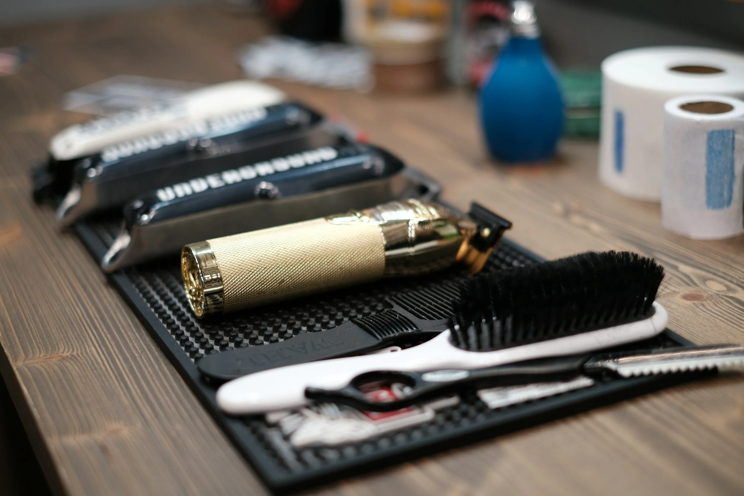 Set of hair clippers, brush, and grooming supplies on a black mat on a wooden surface.