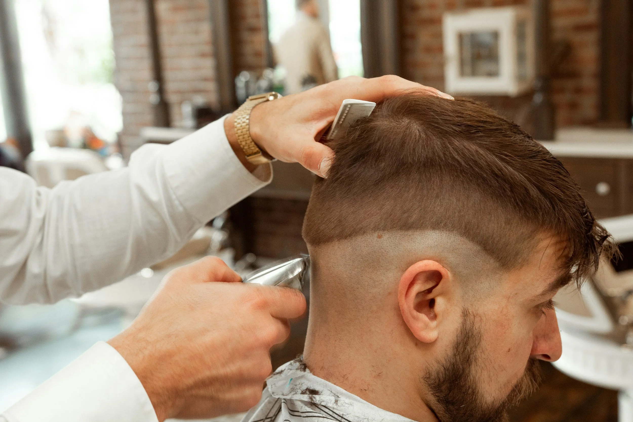 A man getting a haircut at a barber shop, with a barber trimming his hair using clippers.
