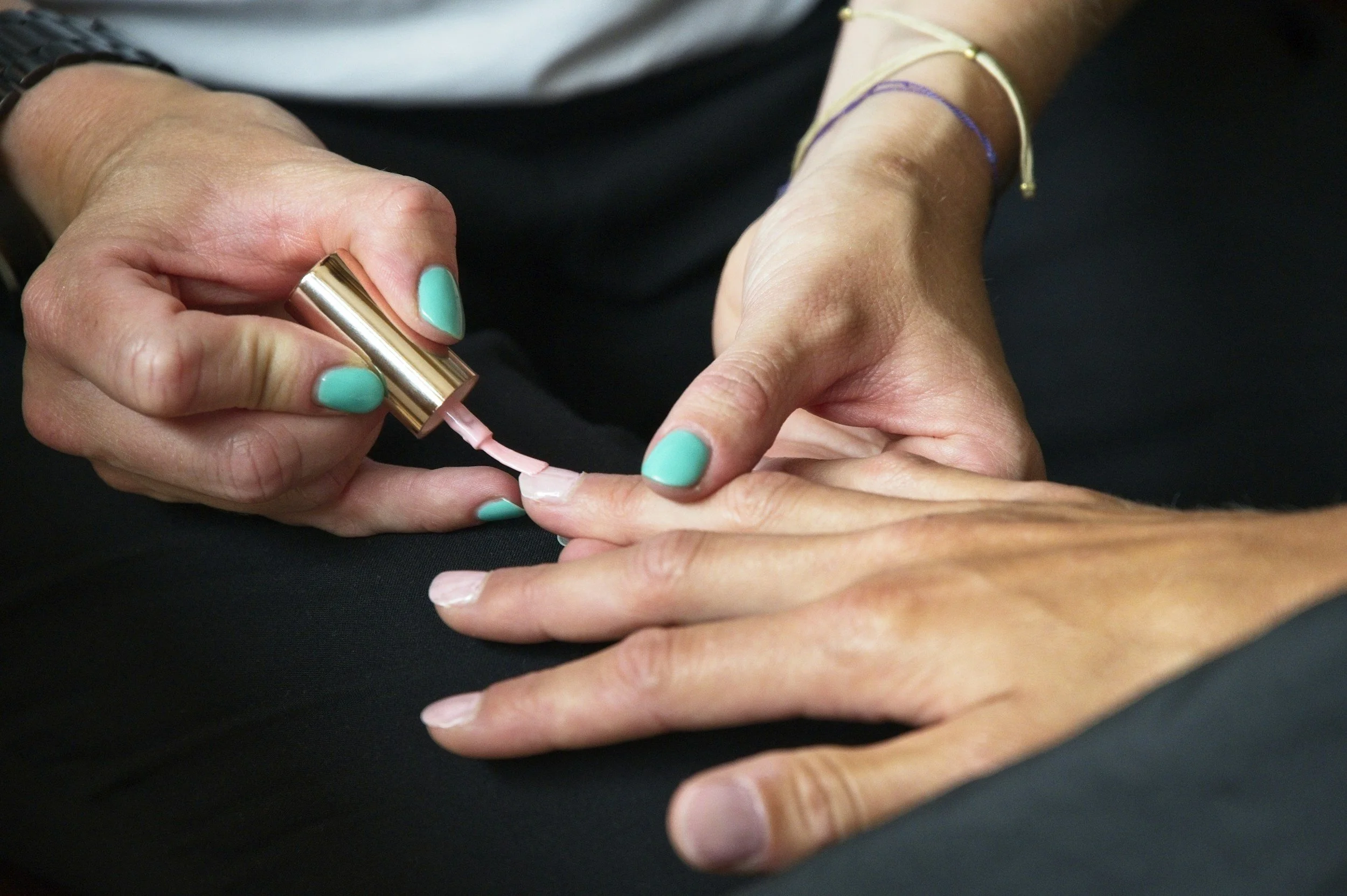 Person applying light pink nail polish on another person's fingernails.