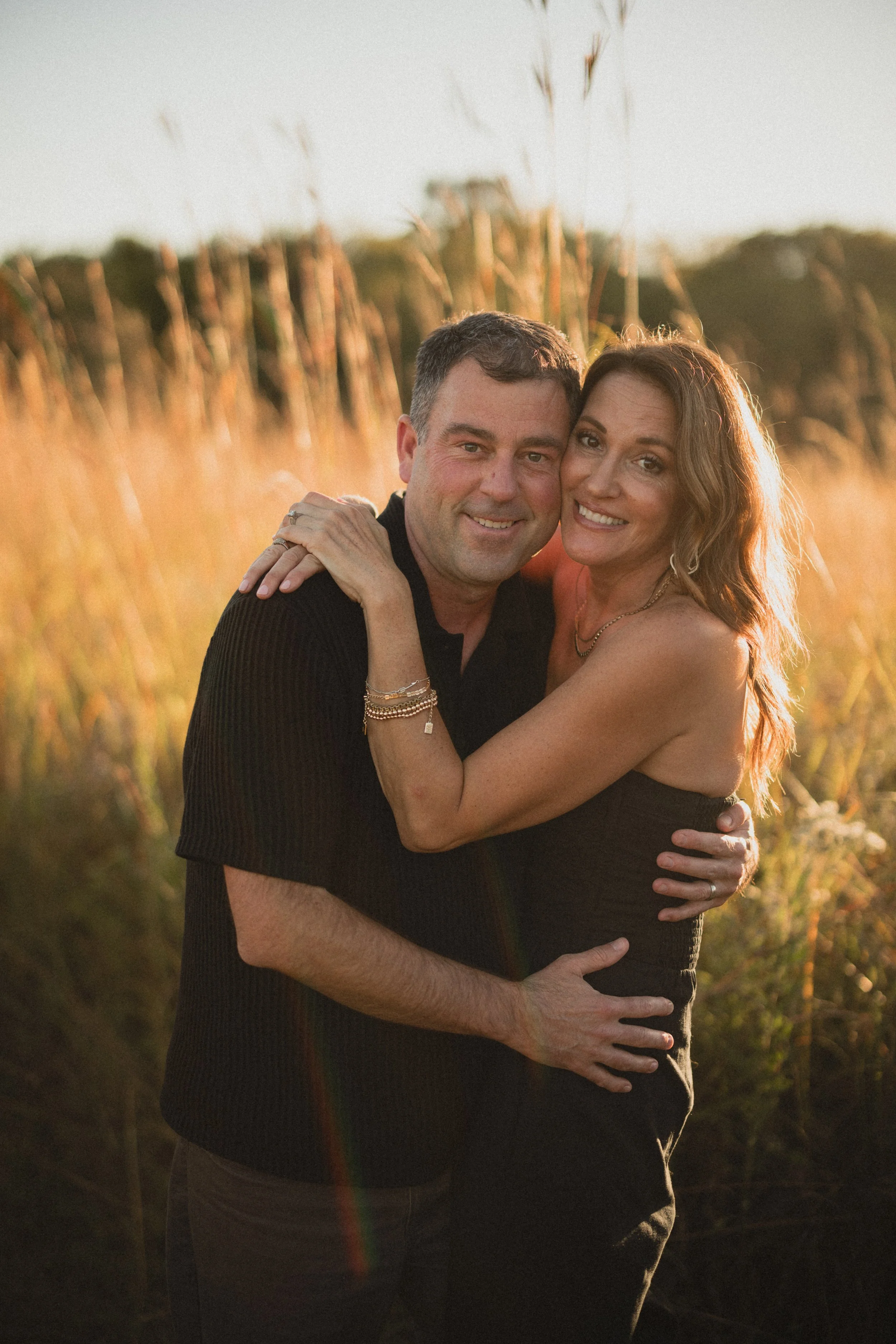 A happy couple embracing outdoors in a field, bathed in warm golden sunlight.