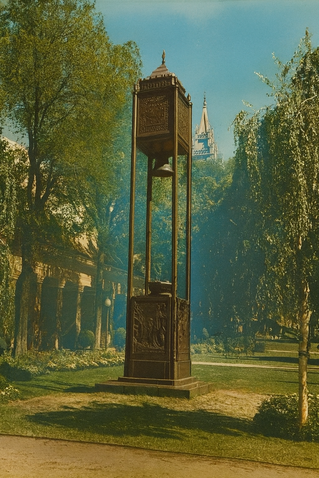 A tall, ornate clock with a bell in Temple Square in Salt Lake City, Utah surrounded by trees and the Mormon Temple in the background.