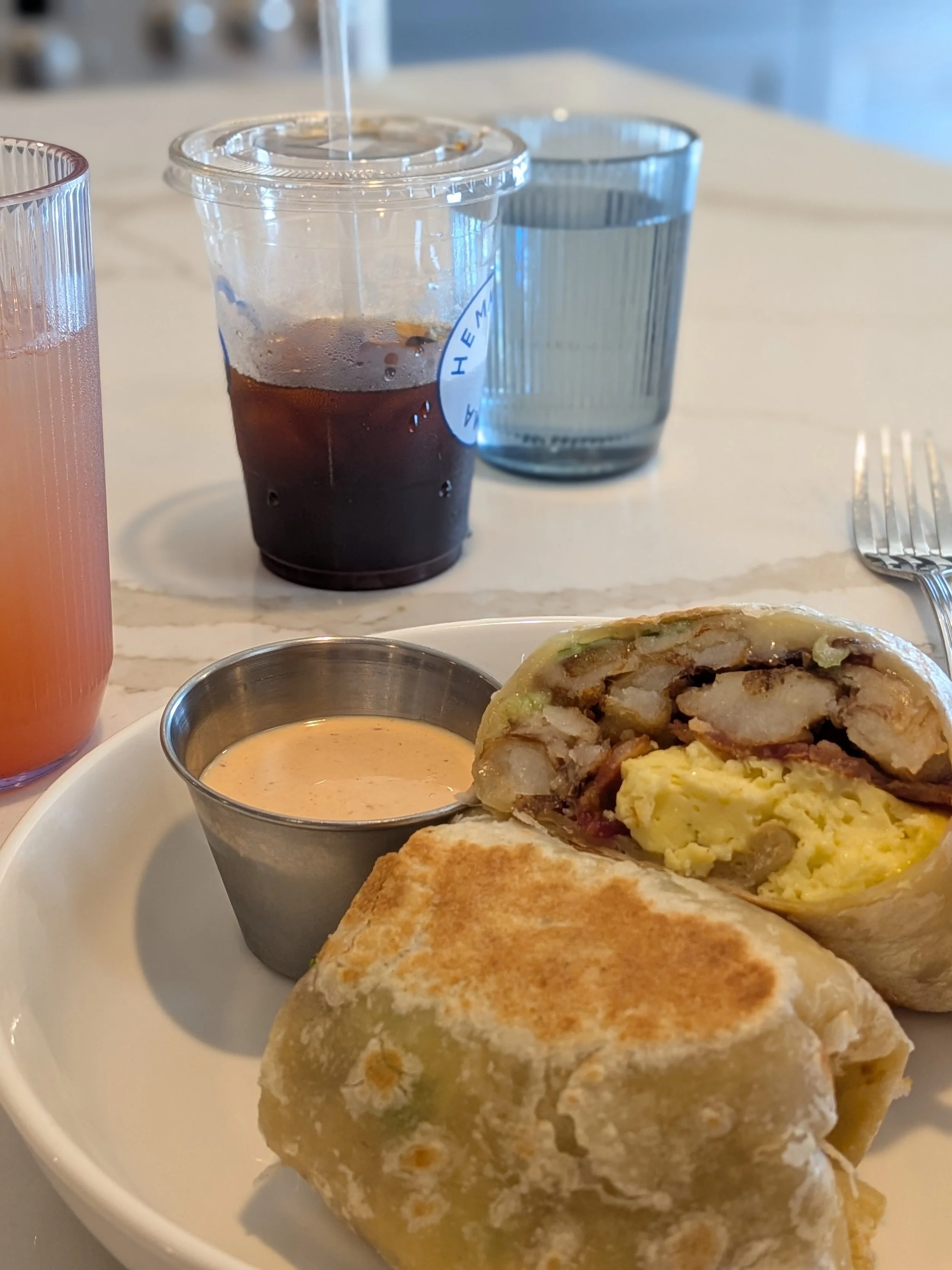 A breakfast burrito with coffee in the background from Hemma Hemma in Kansas City