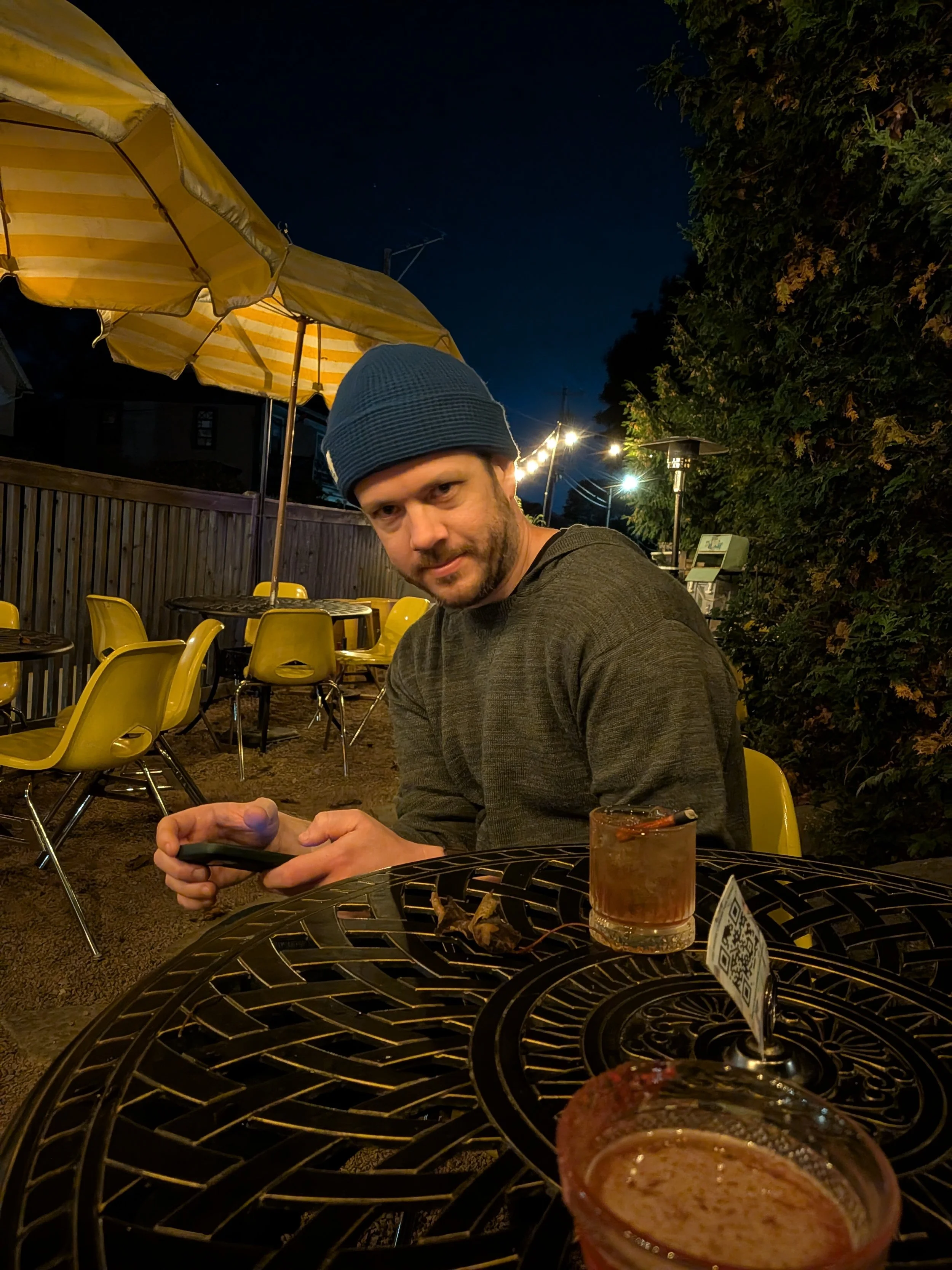 A man in a blue beanie sitting on a patio at night at Project Social in Bar Harbor, Maine.