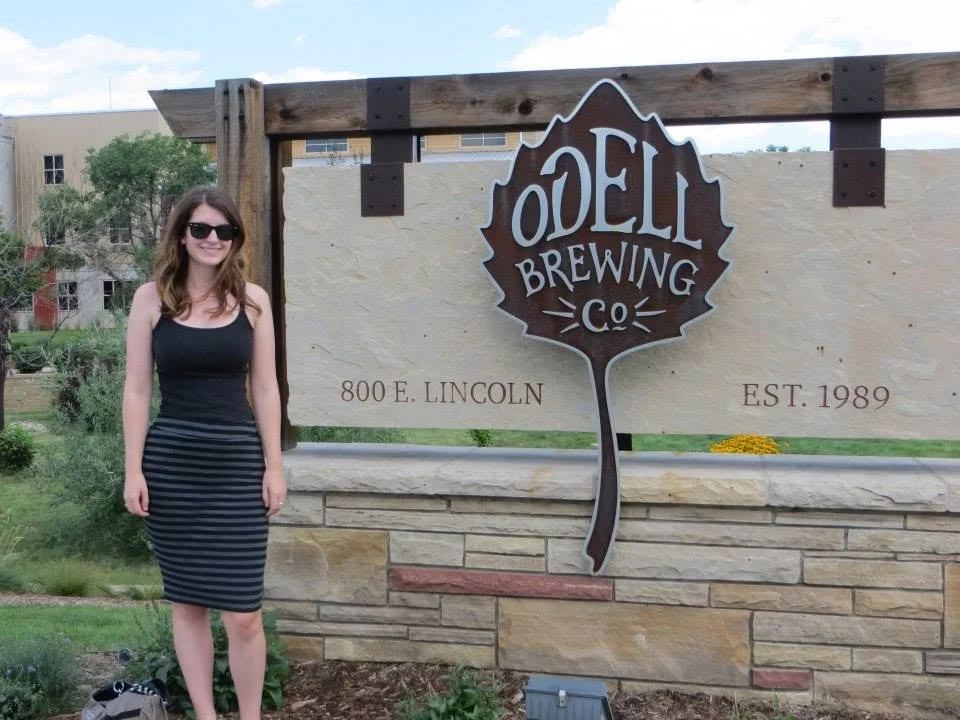 Young woman standing next to a large stone sign for O'Dell Brewing Company.