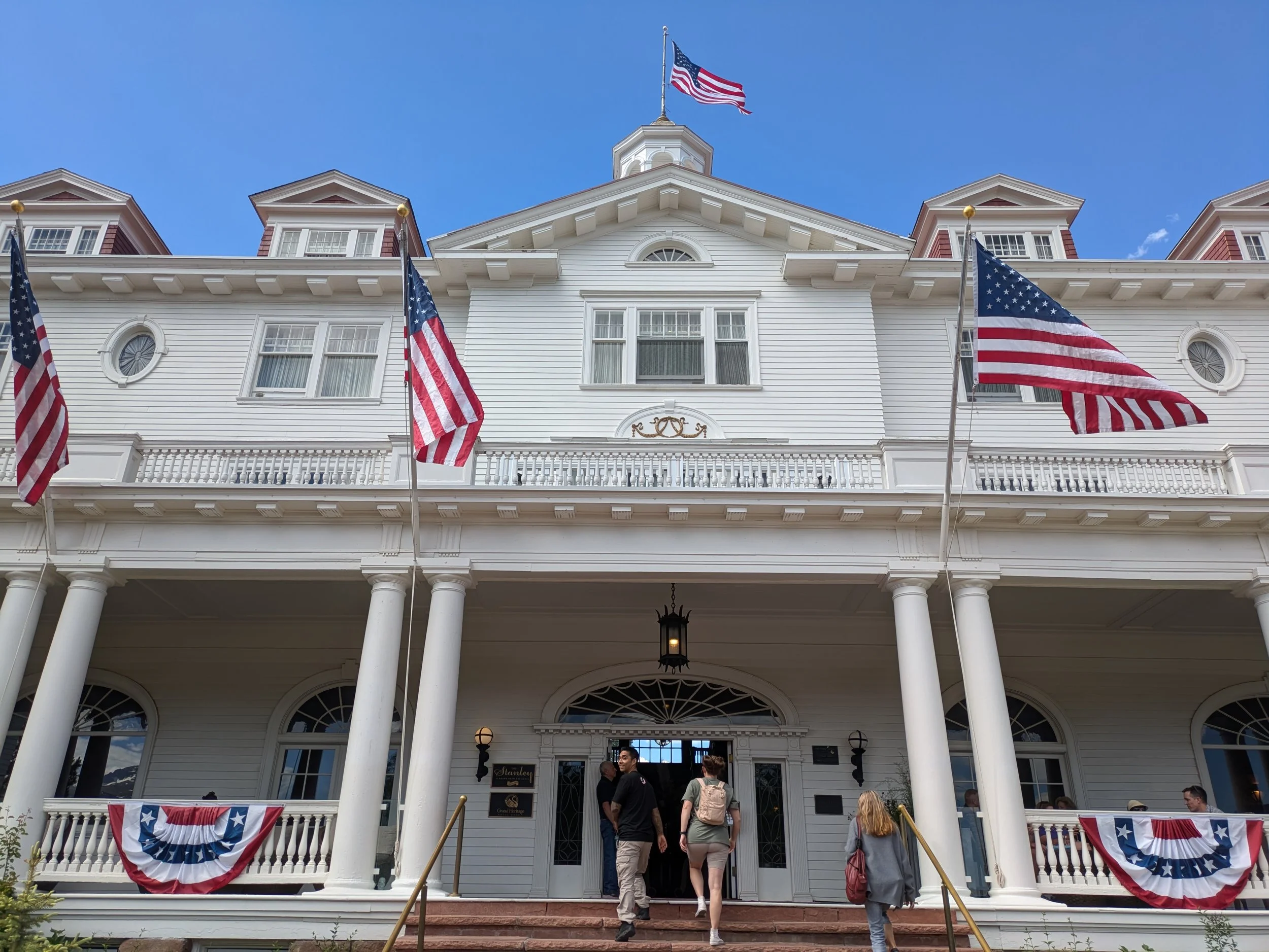 A large white hotel entrance with American flags hanging on flag poles and on banners.