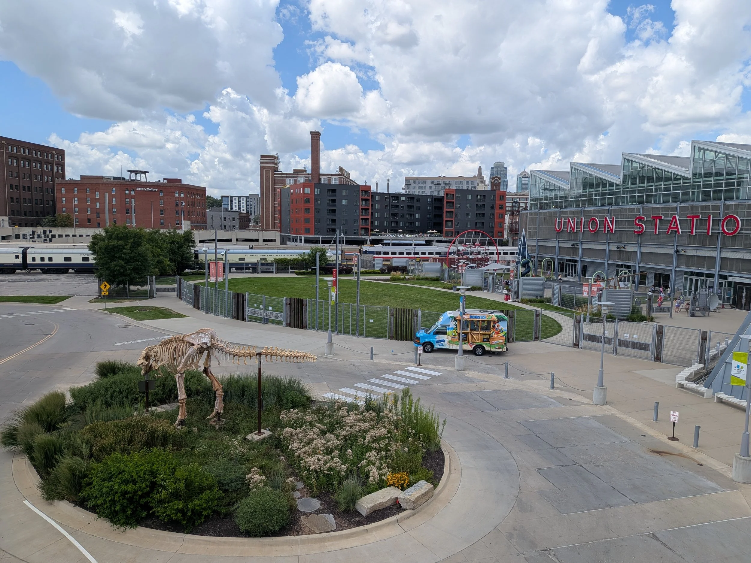 City skyline with Union Station building and sign in the foreground, a small park and dinosaur skeleton.