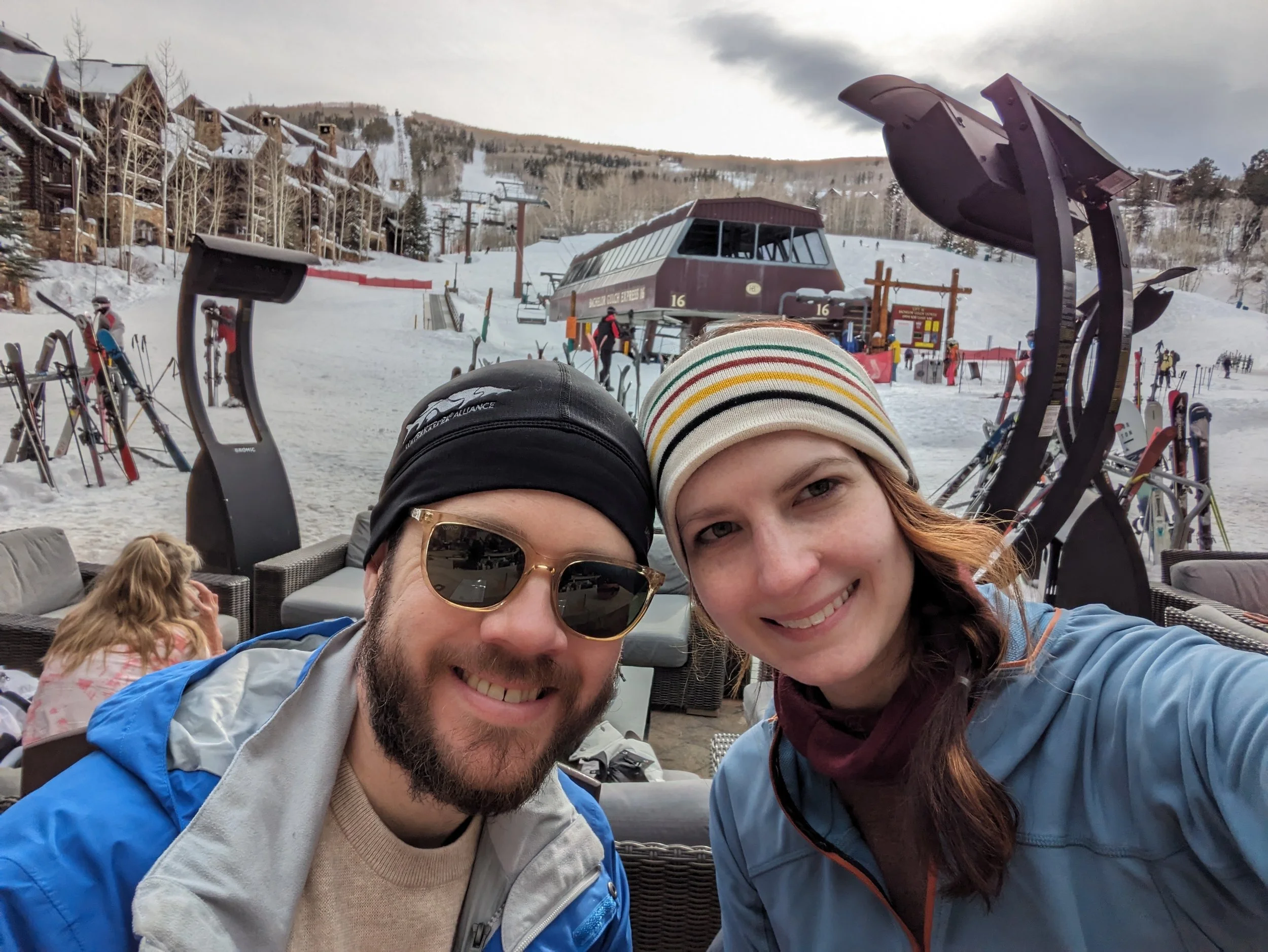 A man and a woman smiling with a ski lift and ski trail in the background.