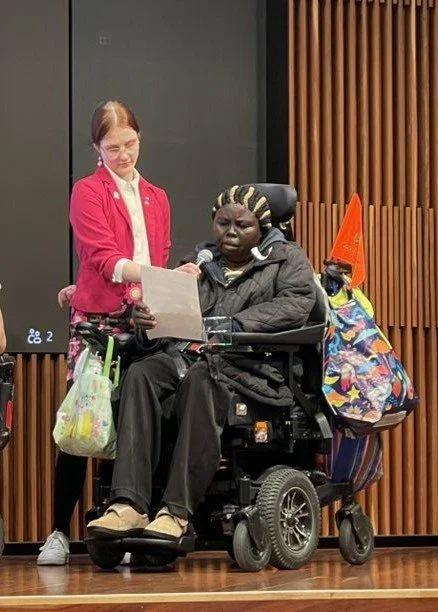A woman in a wheelchair speaks into a microphone held by another woman.