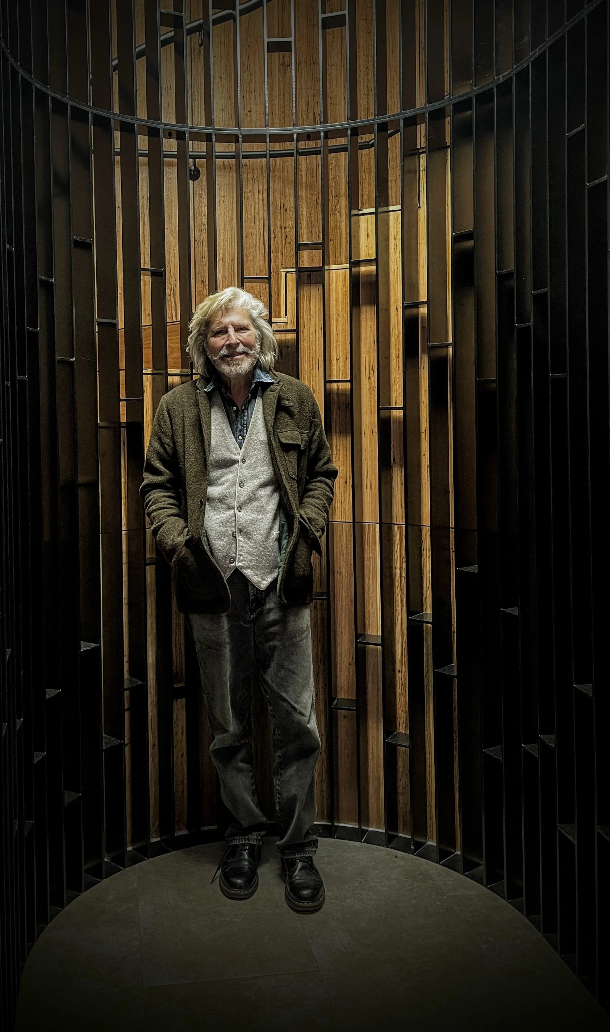 Bill Pezzimenti gray hair and beard standing inside a circular wooden and black metal structure, smiling and posing for the photo.