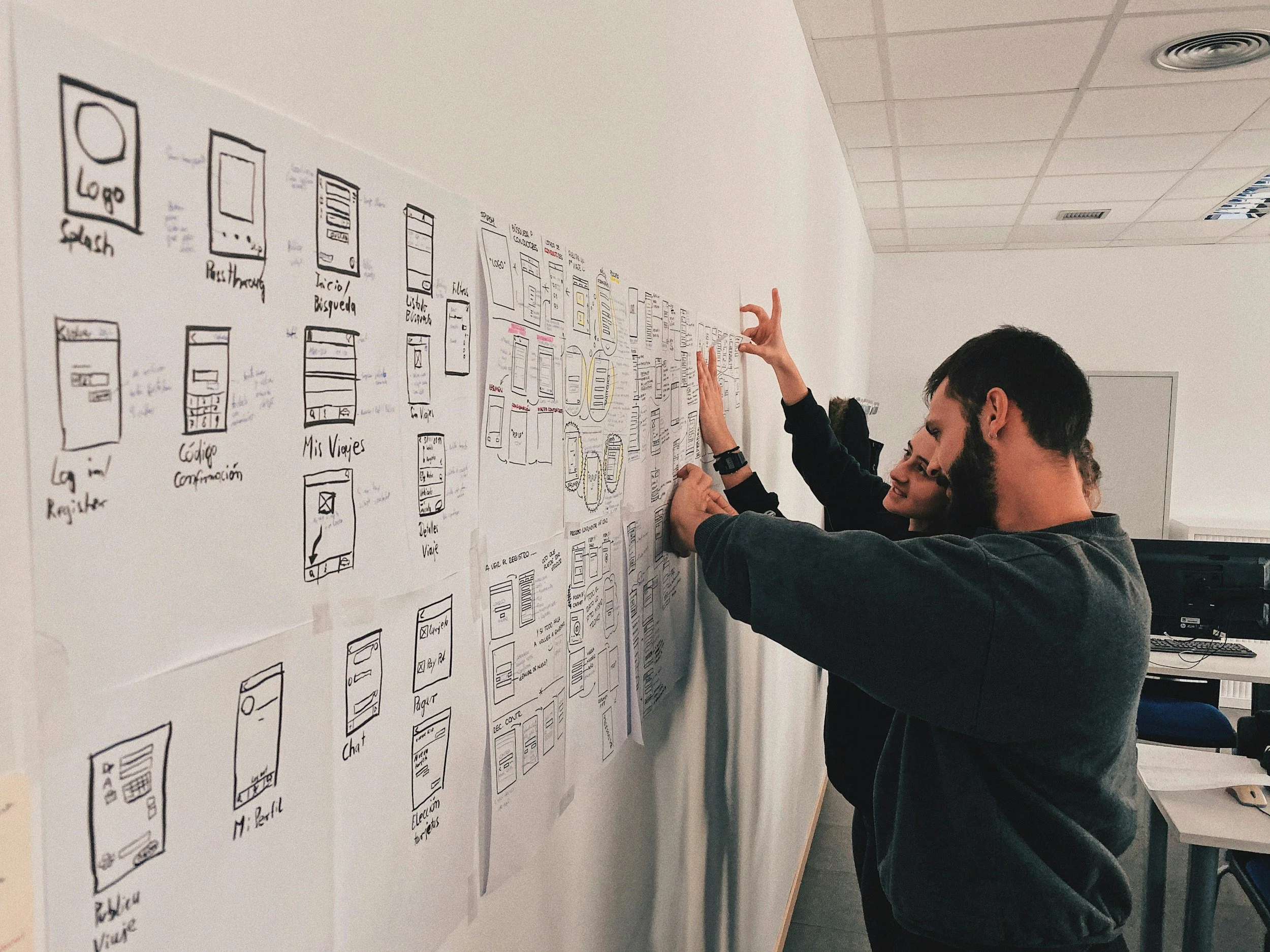 People collaborating on a wireframe storyboard on a wall in an office.