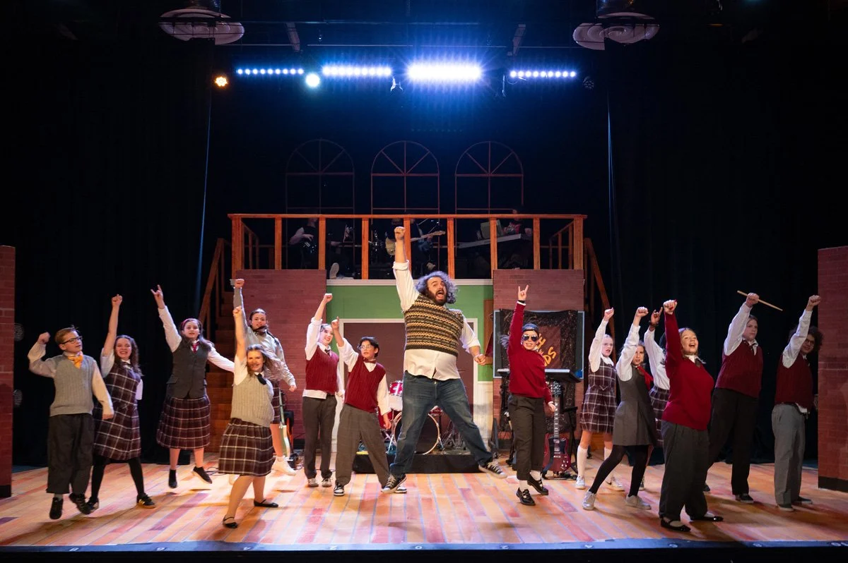 Stage adaptation of School of Rock with cast members jumping in the air.
