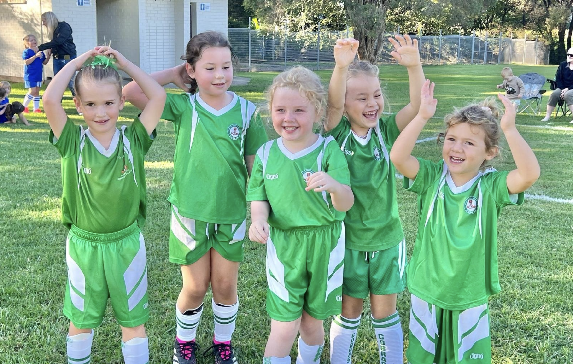 Group of young girls in green soccer uniforms celebrating on a grassy field.