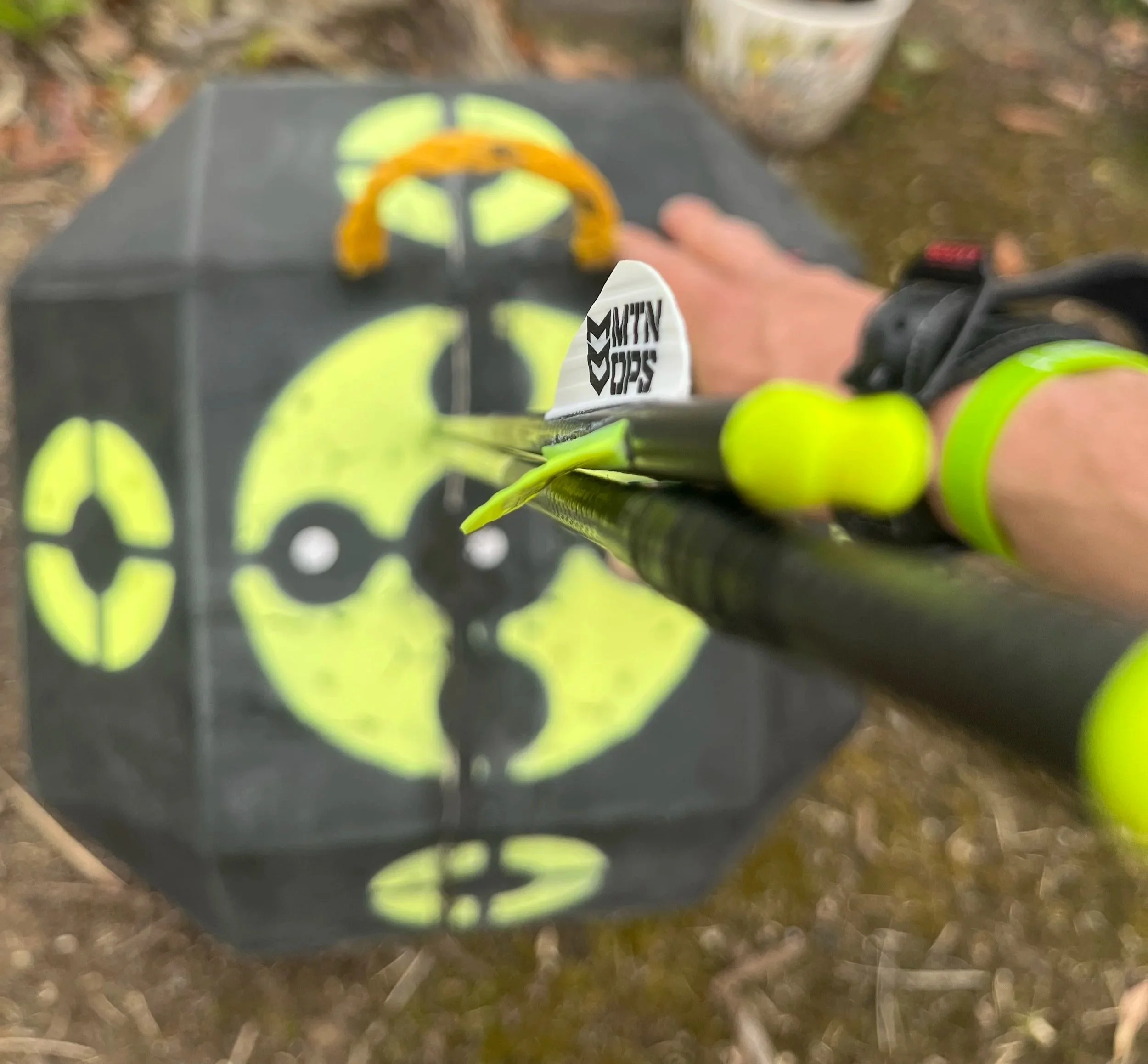 Close-up shot of a person holding a black and yellow target with a white arrow with black writing in focus, while a black and yellow target with a crosshair design in the background is out of focus.