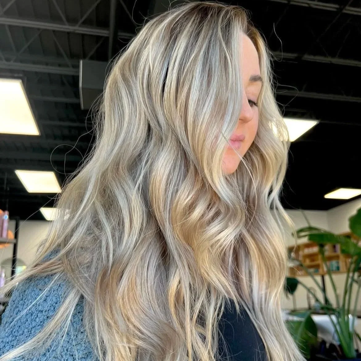 Side profile of a woman with long, wavy blonde hair in an indoor setting.