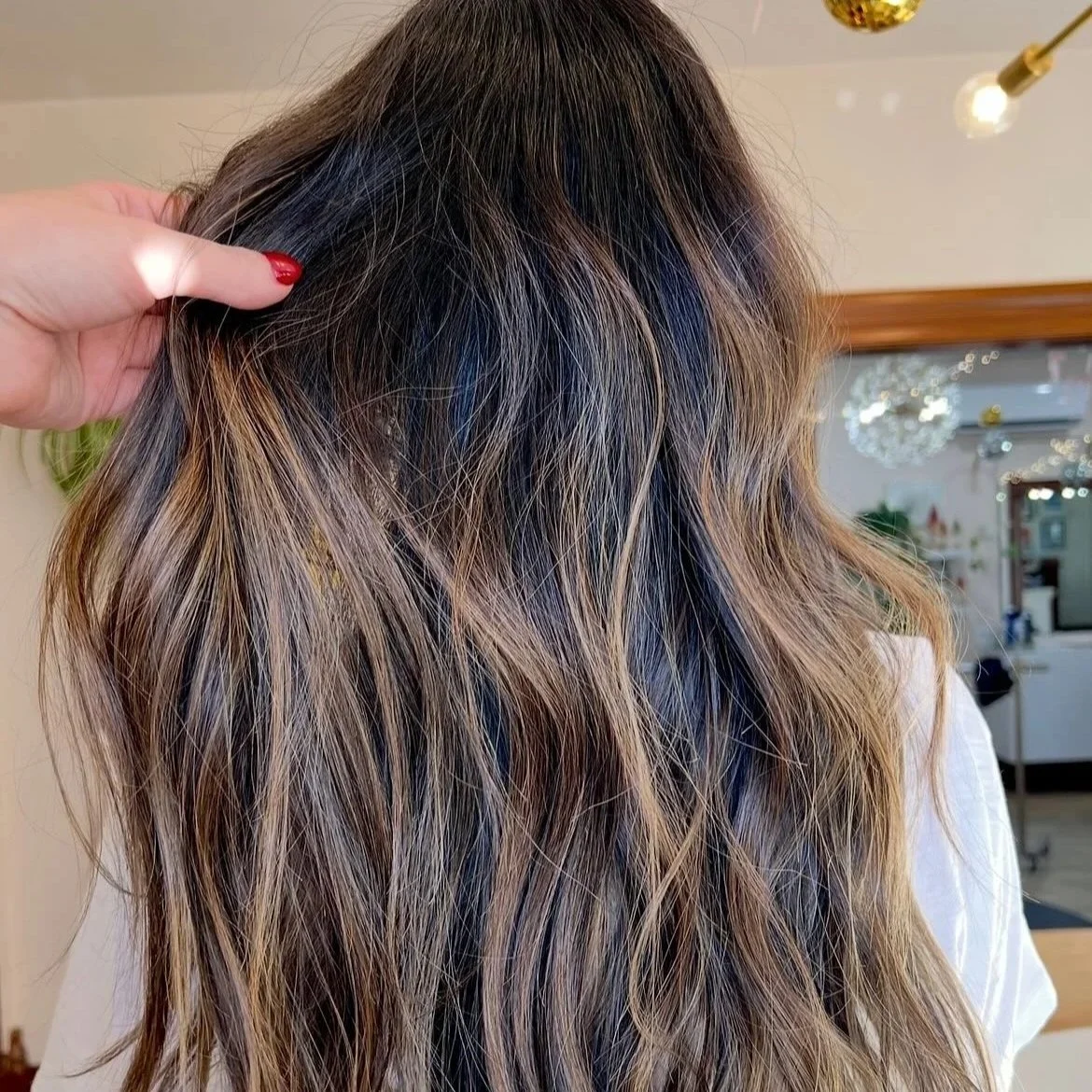 Close-up of a woman's wavy hair with highlights in a salon or home setting.