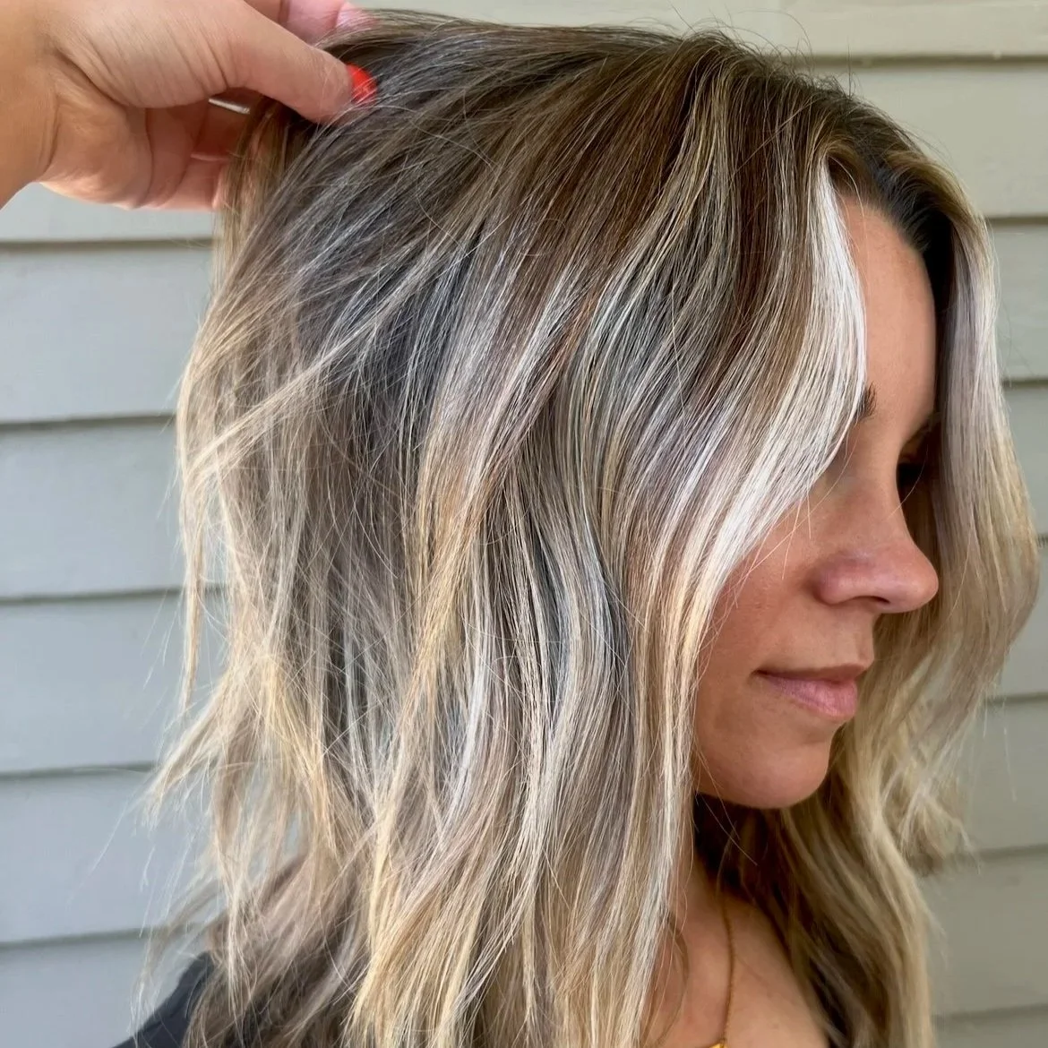 Close-up of a woman with shoulder-length blonde hair with light highlights, gently touching her hair with her hand.