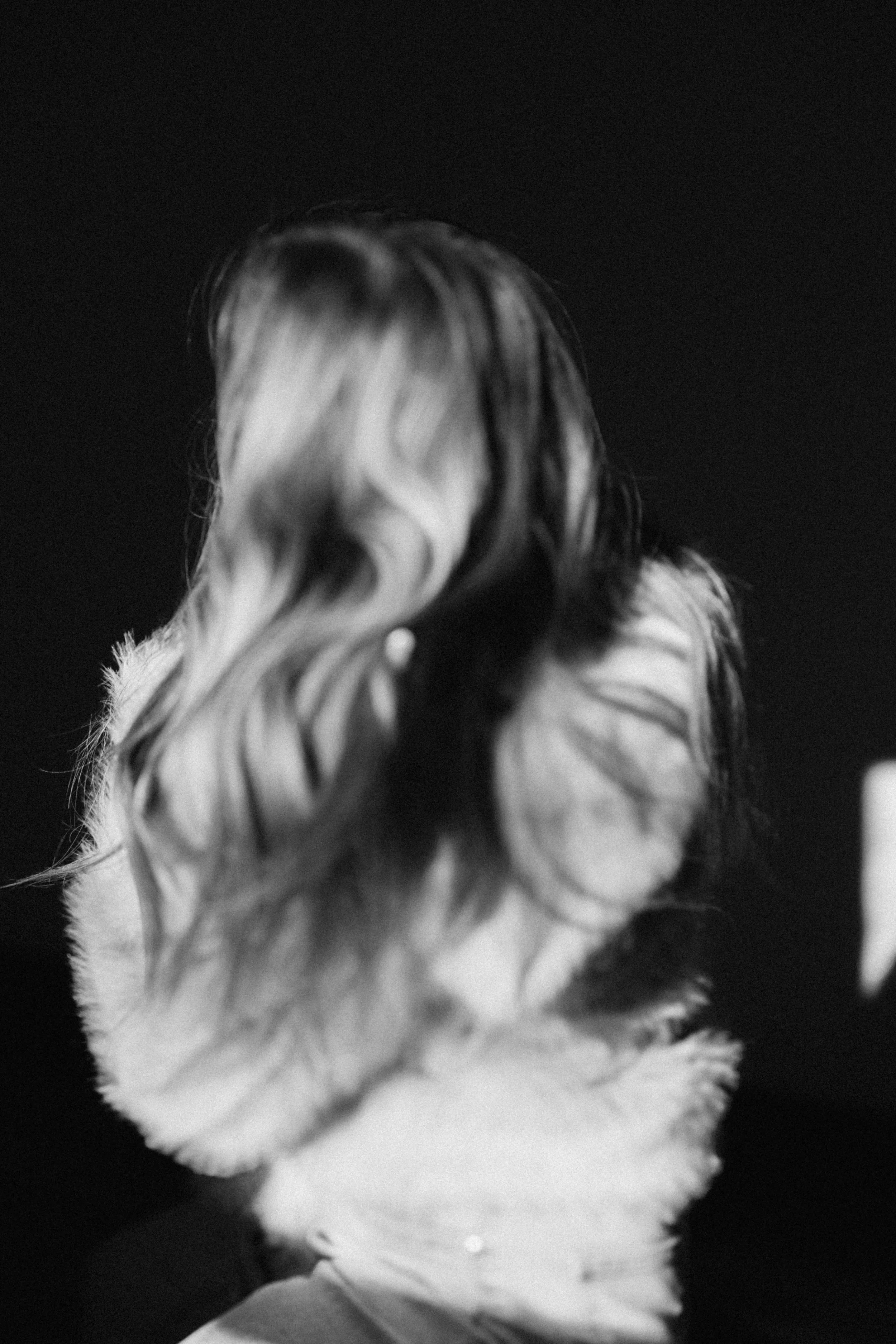 Black and white photograph of two women with wavy hair facing each other, with the focus on their hair and shoulders, against a dark background.