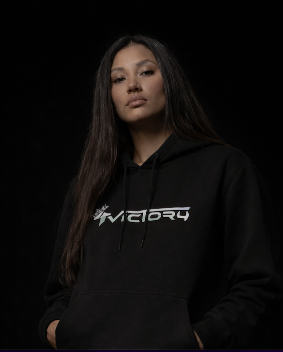 Jeune femme portant un sweat à capuche noir avec le logo '4Victory' blanc, pose contre un fond noir, expression sérieuse.