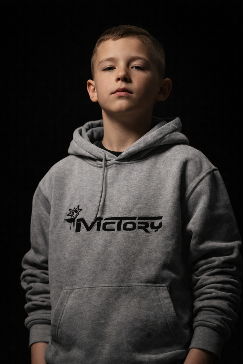Jeune garçon portant un sweat gris avec le mot '4Victory' et un logo stylisé, debout contre un fond noir.