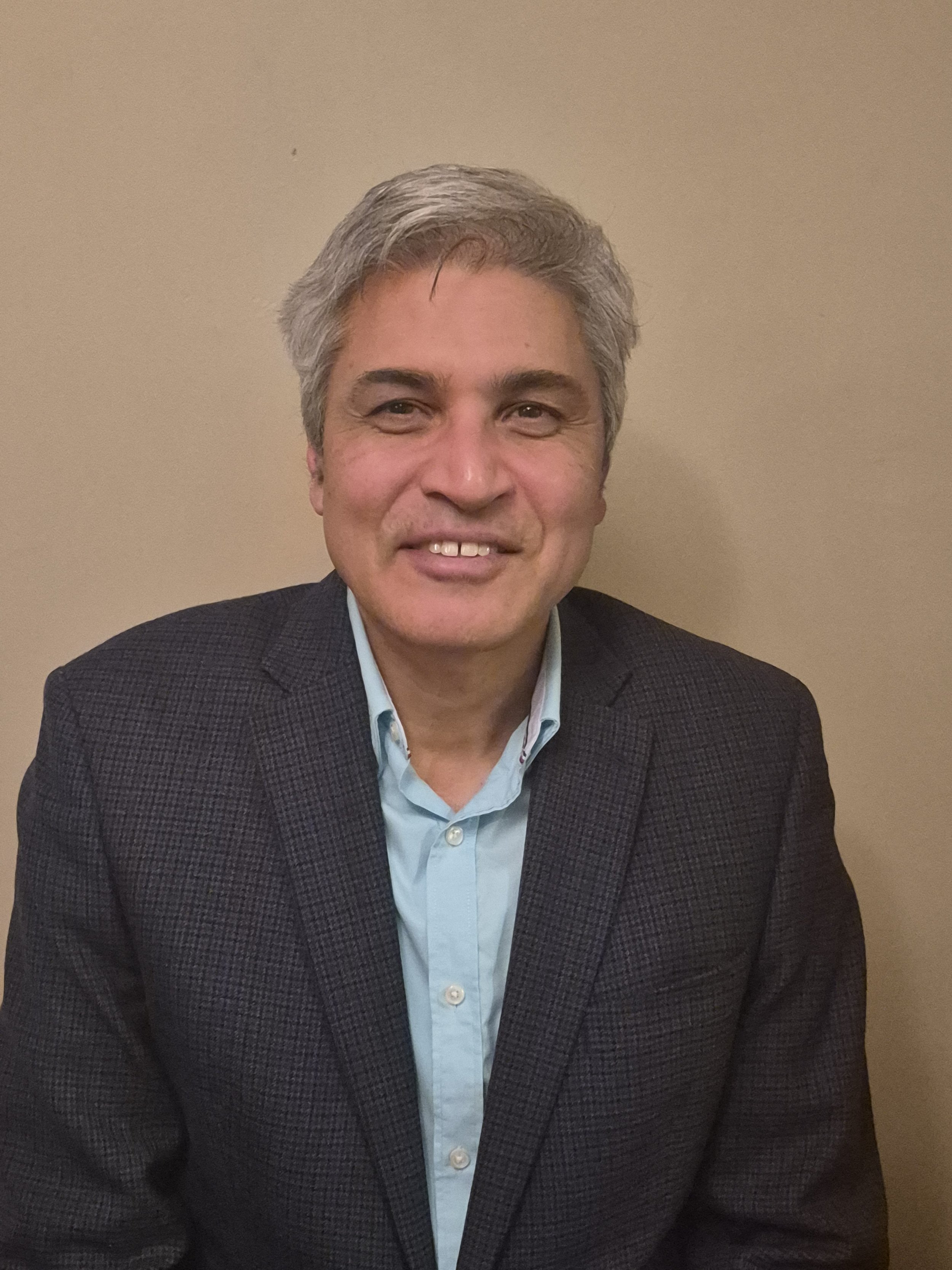 A woman with short blonde hair, wearing an orange sleeveless top and beige pants, sitting on a bench and writing in a notebook in a room with natural light and minimal decor.