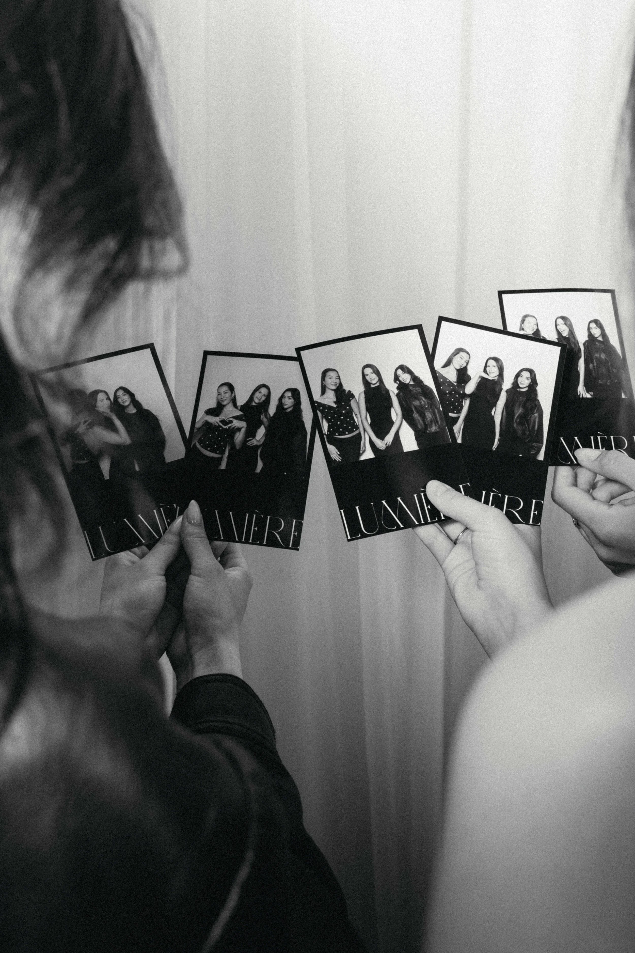 Person holding four black and white photo cards with images of three women in black outfits, while another person holds the other card, all photos featuring the same women posing together.
