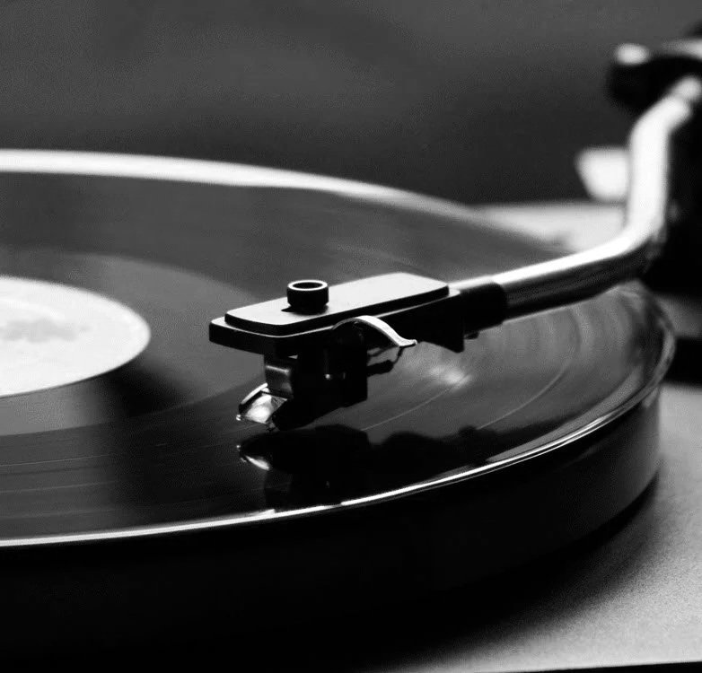 A black and white close-up of a vinyl record player with the tonearm resting on a spinning record.
