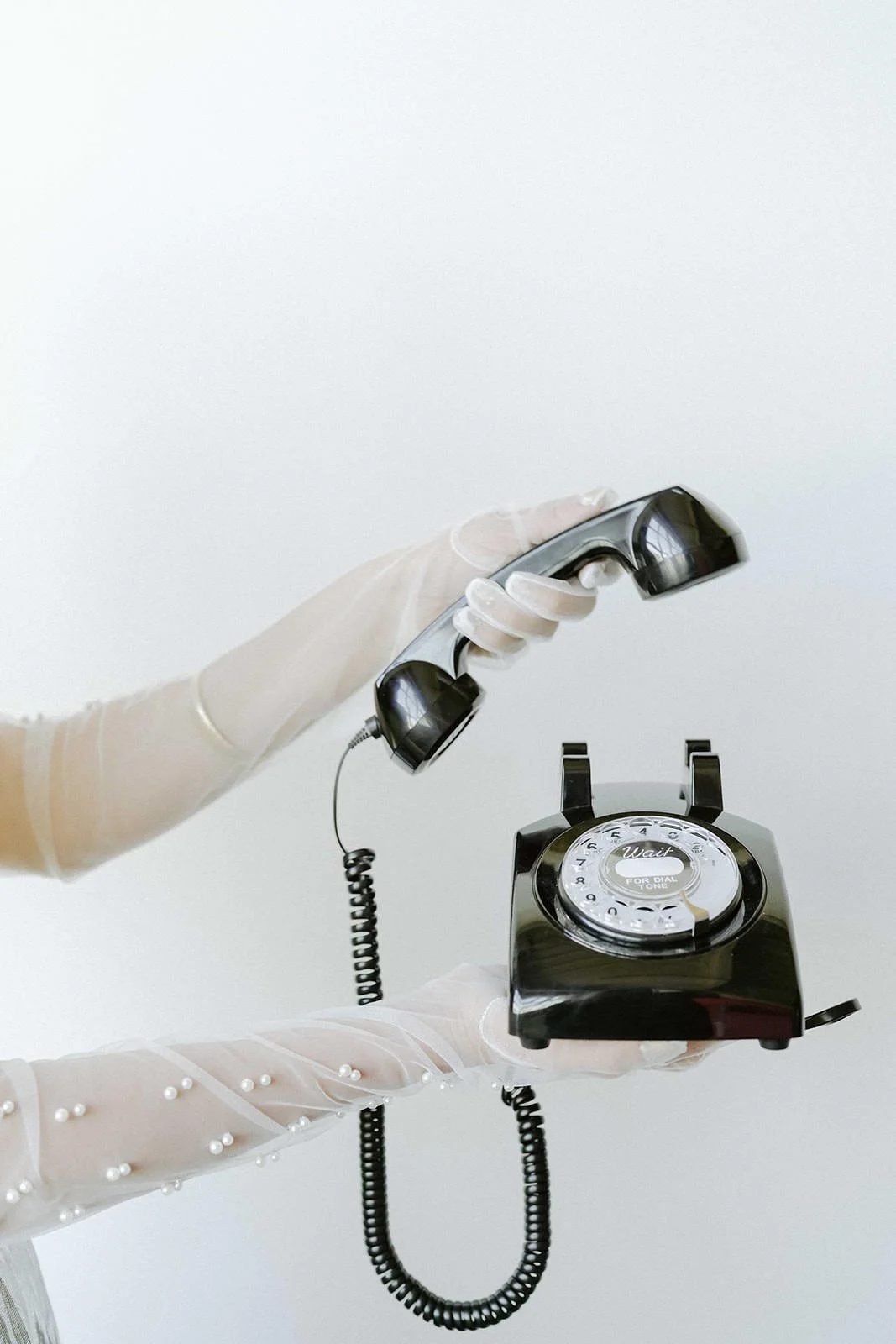 Person wearing gloves holding a vintage black rotary telephone.
