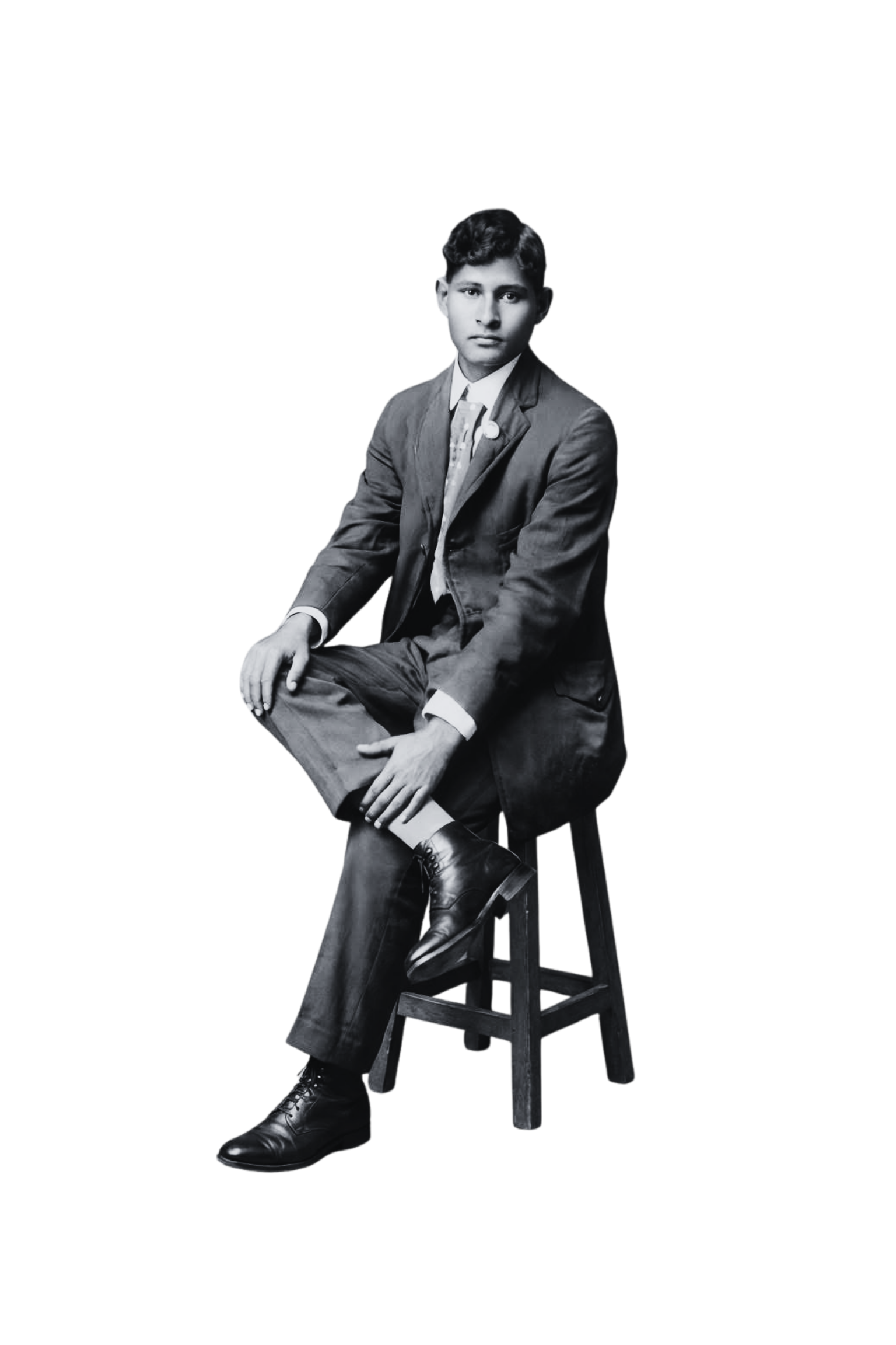 Black and white photo of a young man sitting on a stool, dressed in vintage attire including a suit and tie, with a serious expression.
