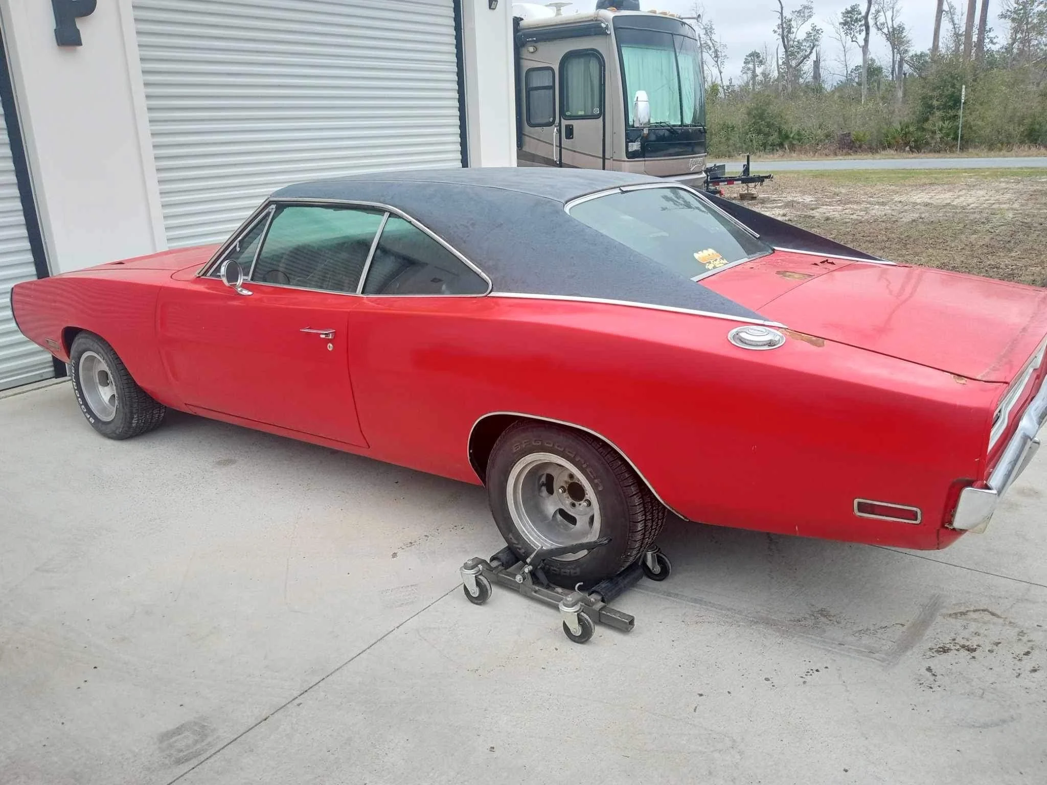 A red vintage car with a black roof, parked outside near a garage with a closed metal door, on a concrete driveway. This car had no title, but obtained one by using classictitleworks.com