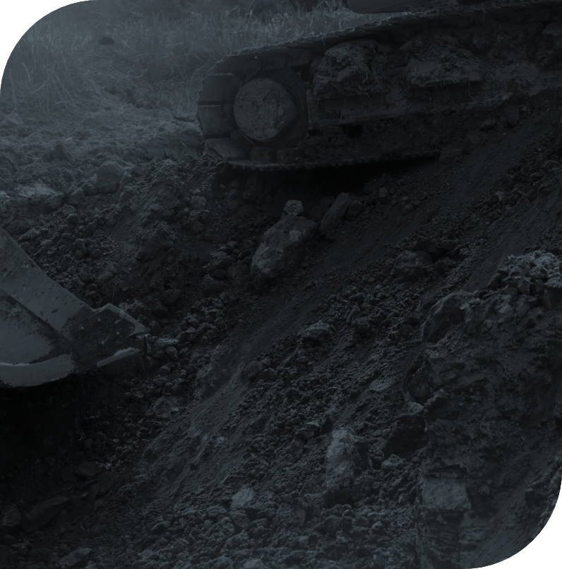 Close-up of a construction site showing an excavator bucket digging into the dirt with rocks and soil.