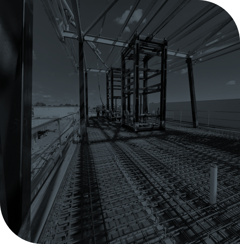 Construction site with steel framework and safety railing, overlooking bodies of water and a partly cloudy sky.