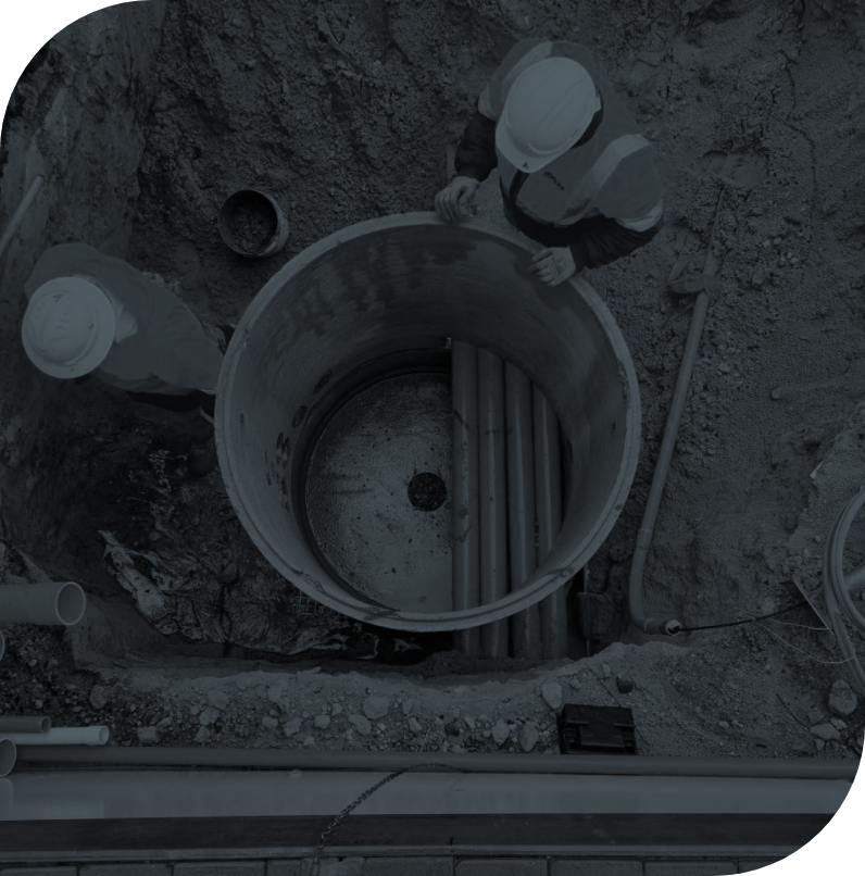 Workers in hard hats inspecting a large underground utility vault with pipes inside.