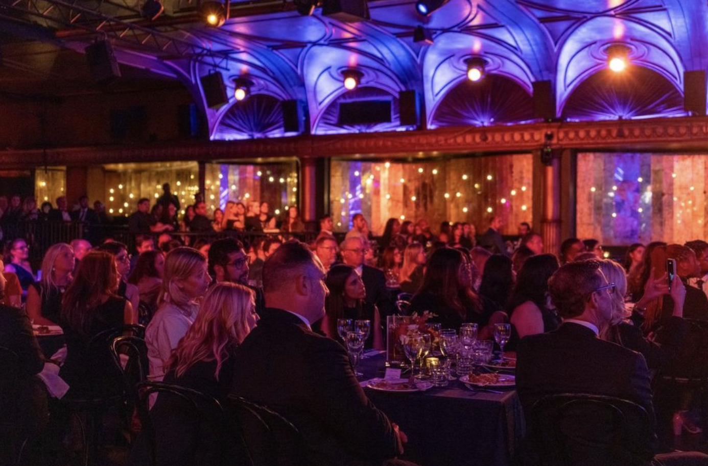 Audience attending an indoor event with colorful lighting and decorated walls.