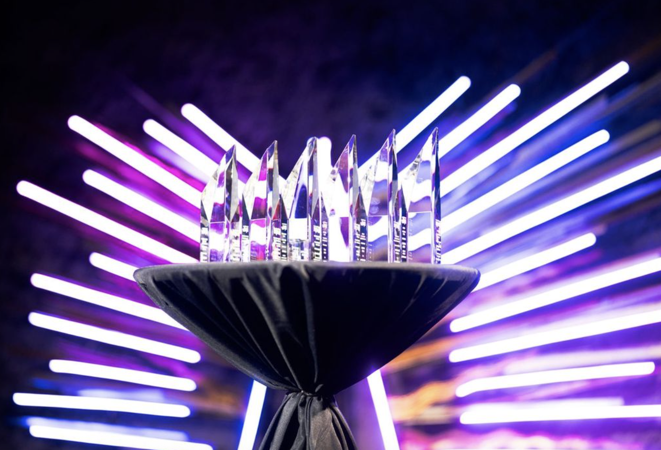 A clear crystal award with multiple pointed peaks on a black satin-covered base, illuminated by purple and white neon lights in the background.