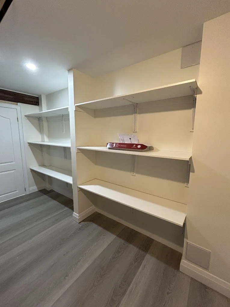Empty white shelves on a wall in a room with grey wood flooring.