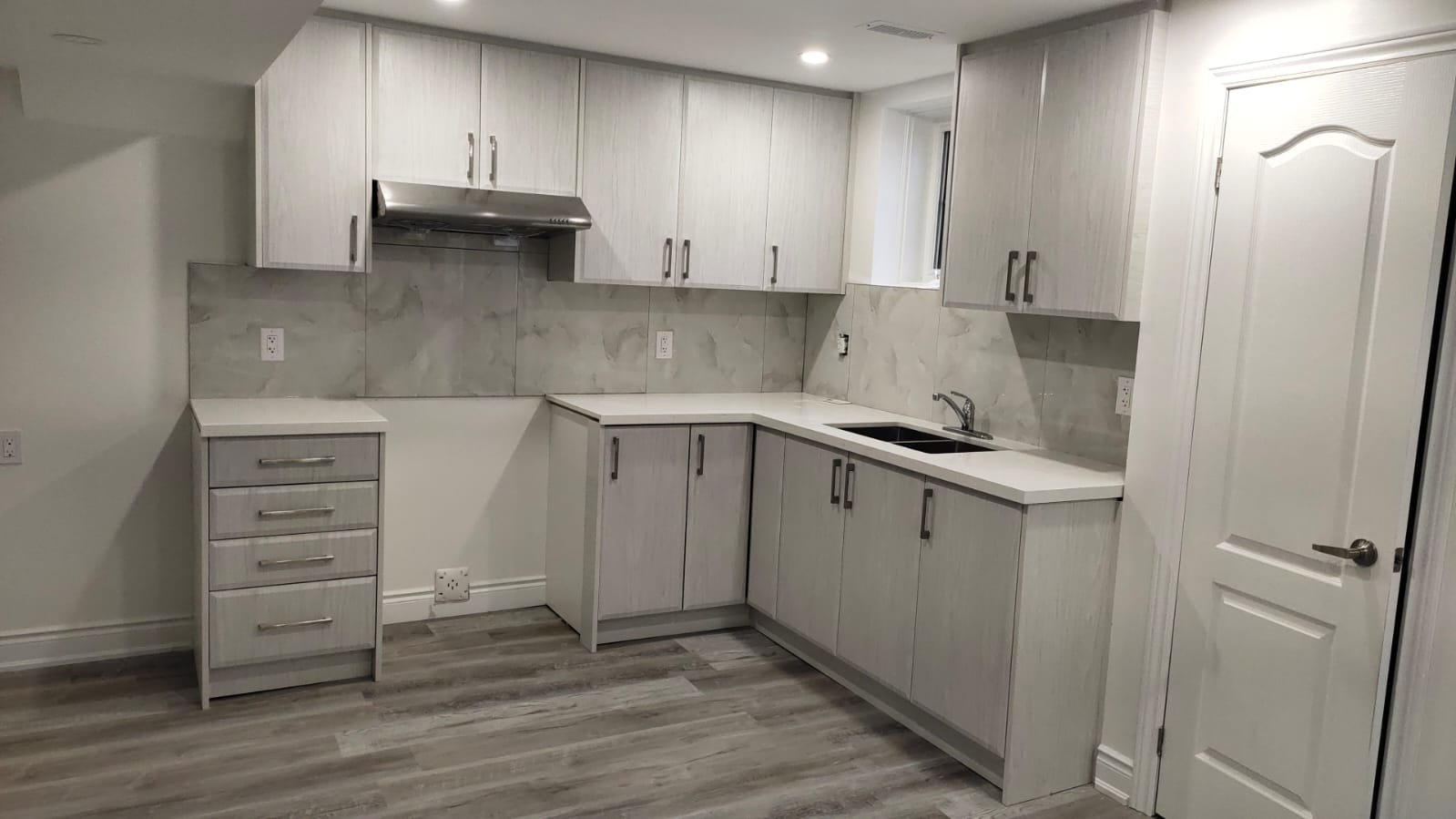 Kitchen with white cabinets, marble backsplash, gray flooring, built-in sink, and a door on the right.
